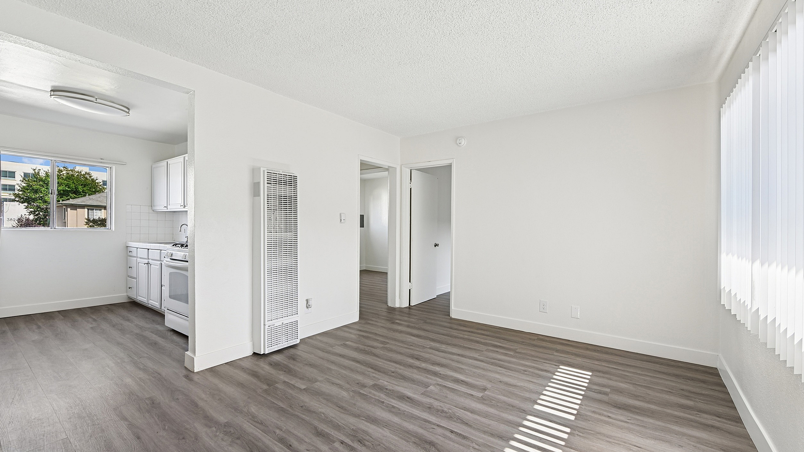 Bright and airy apartment interior with modern laminate flooring, featuring a cozy kitchen nook and abundant natural light from large windows.