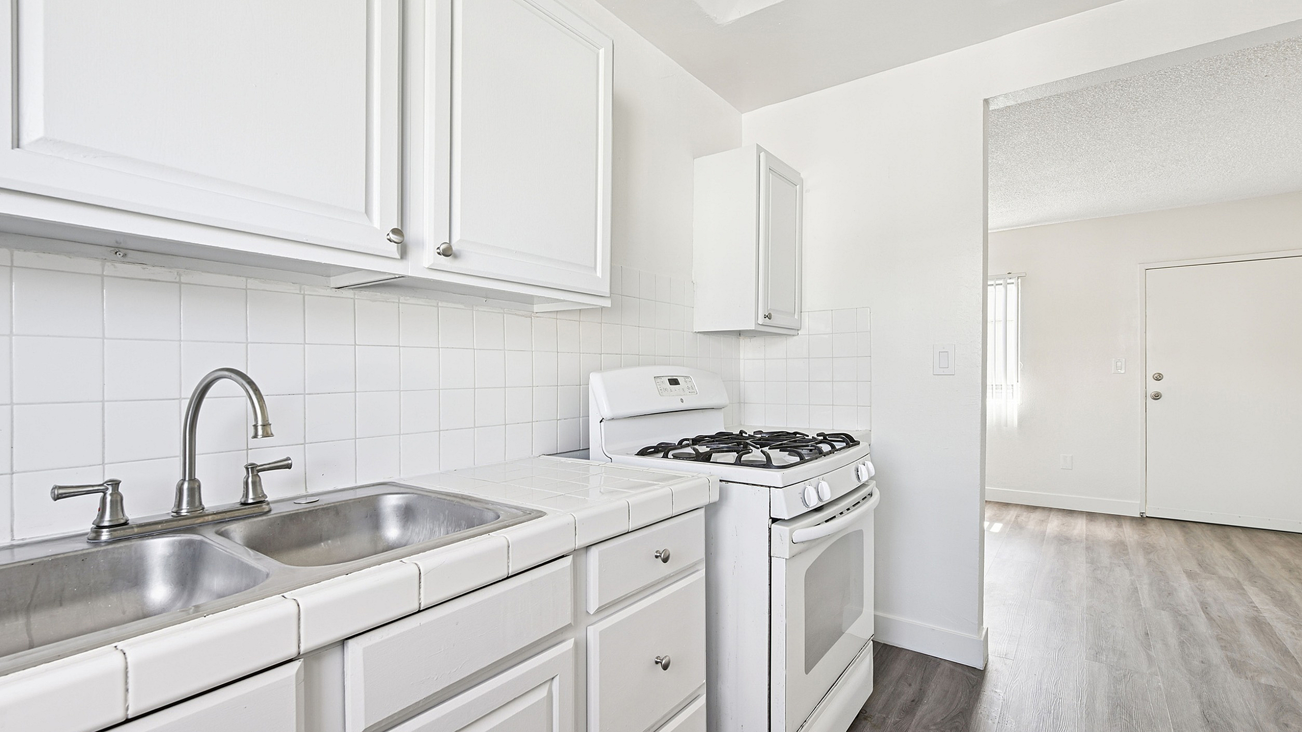 Bright and inviting kitchen with white cabinetry, modern fixtures, and a sleek gas stove opening into a sunlit living area.
