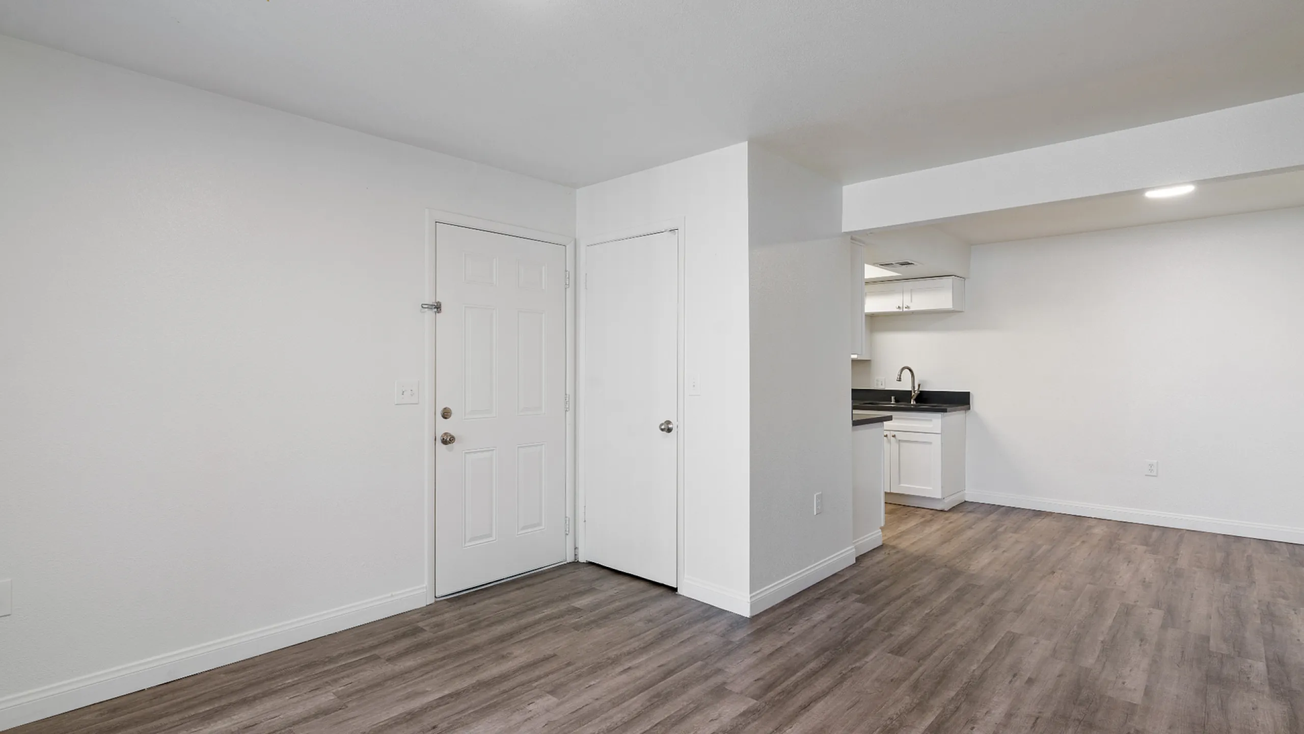 Modern living space with sleek wood flooring, bright white walls, and an inviting open-plan kitchen.