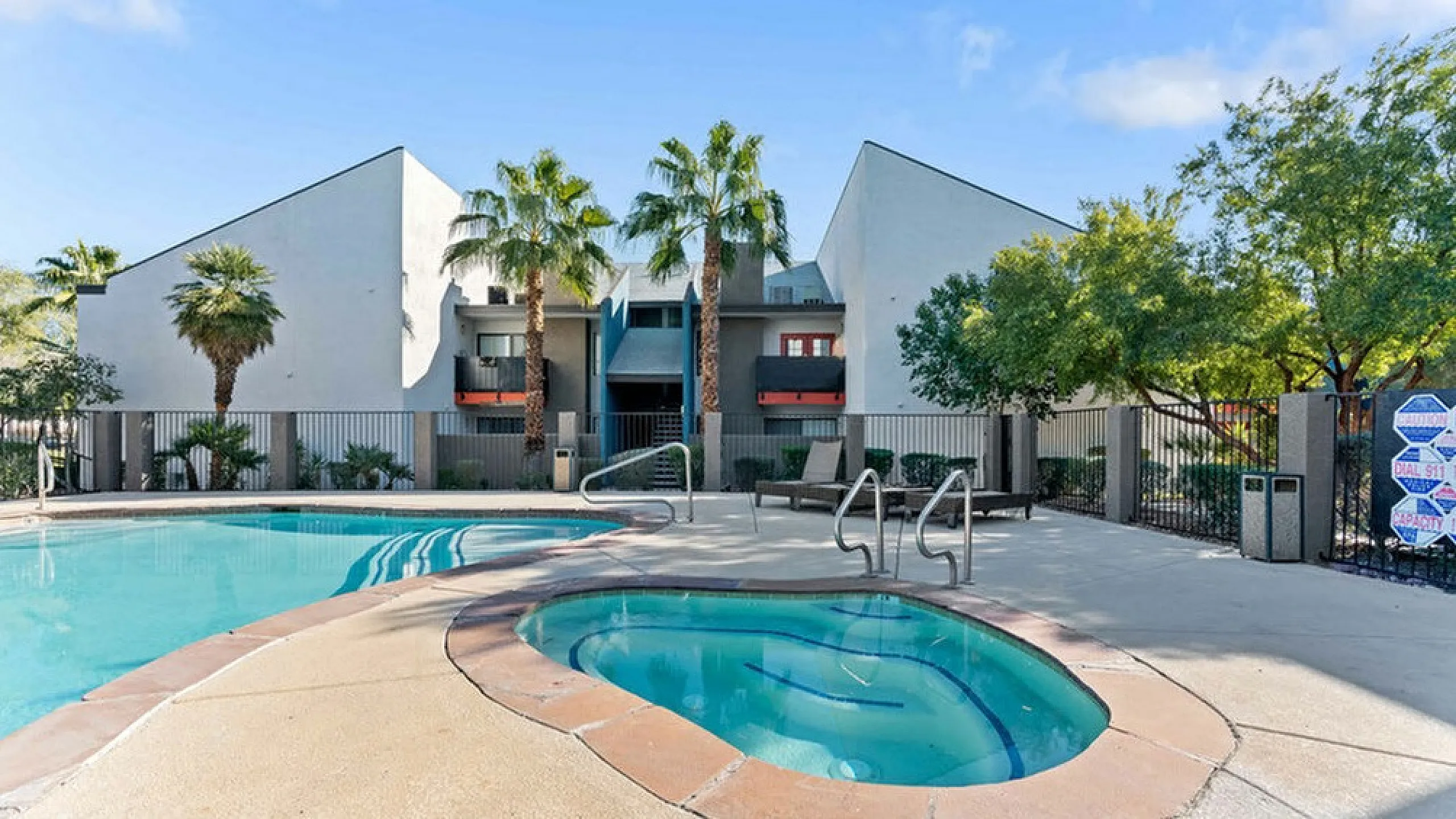 Inviting apartment complex exterior with a refreshing pool and hot tub surrounded by lush palm trees and modern architecture.
