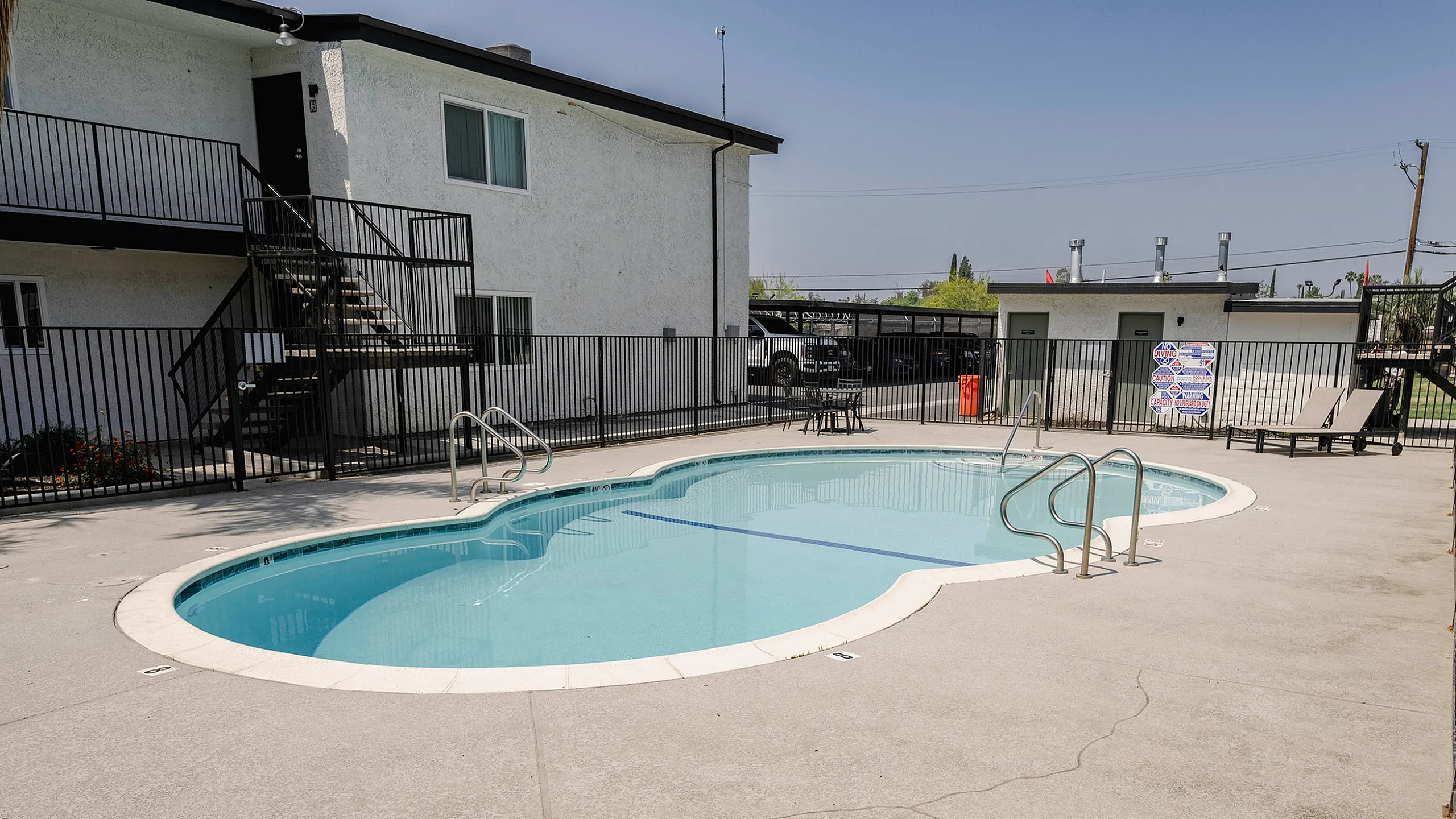 Inviting apartment complex with a sparkling swimming pool, modern loungers, and convenient outdoor seating, perfect for relaxation and leisure.