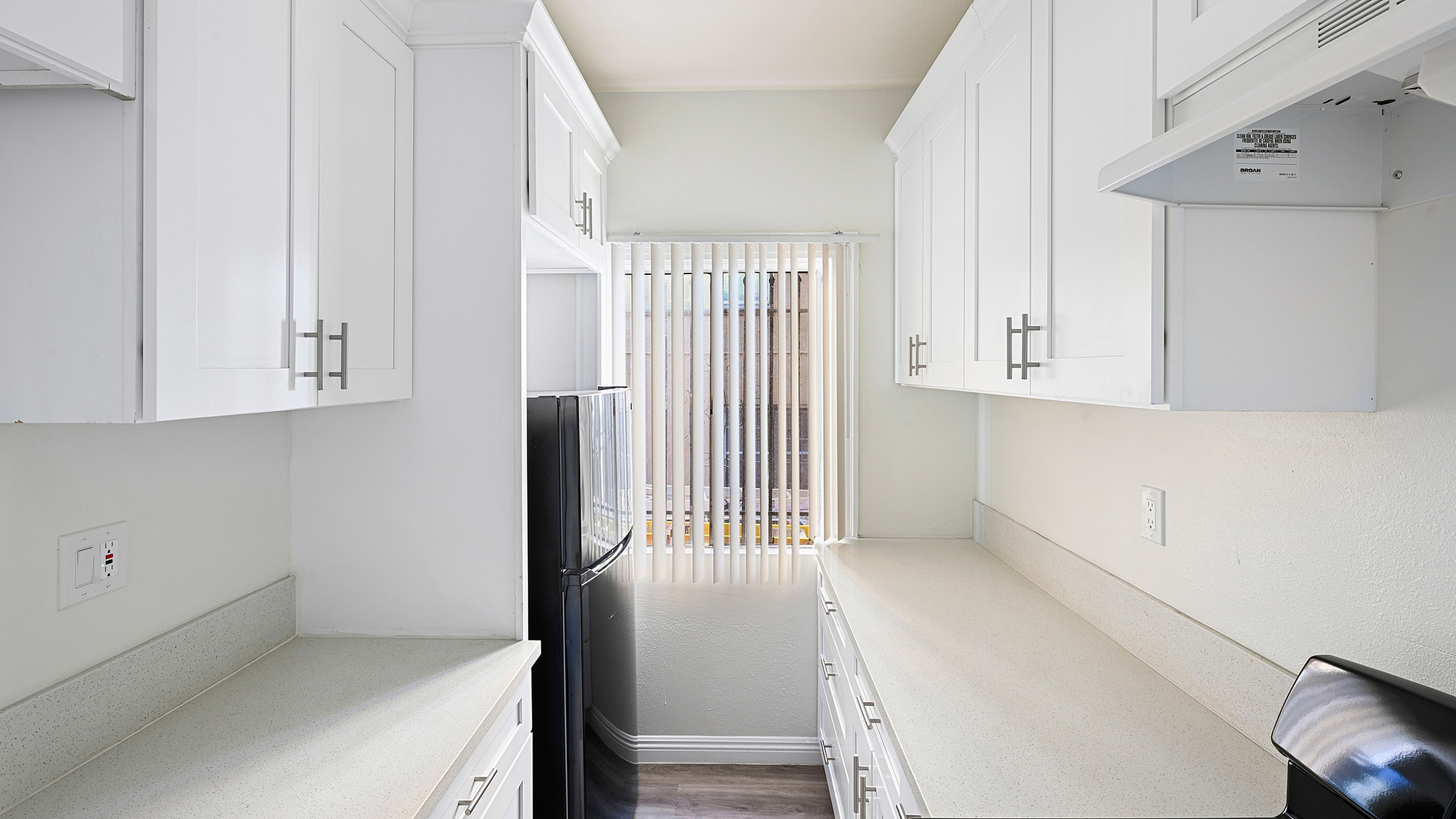 Sleek modern kitchen with pristine white cabinetry, elegant countertops, and ample natural light streaming through vertical blinds.