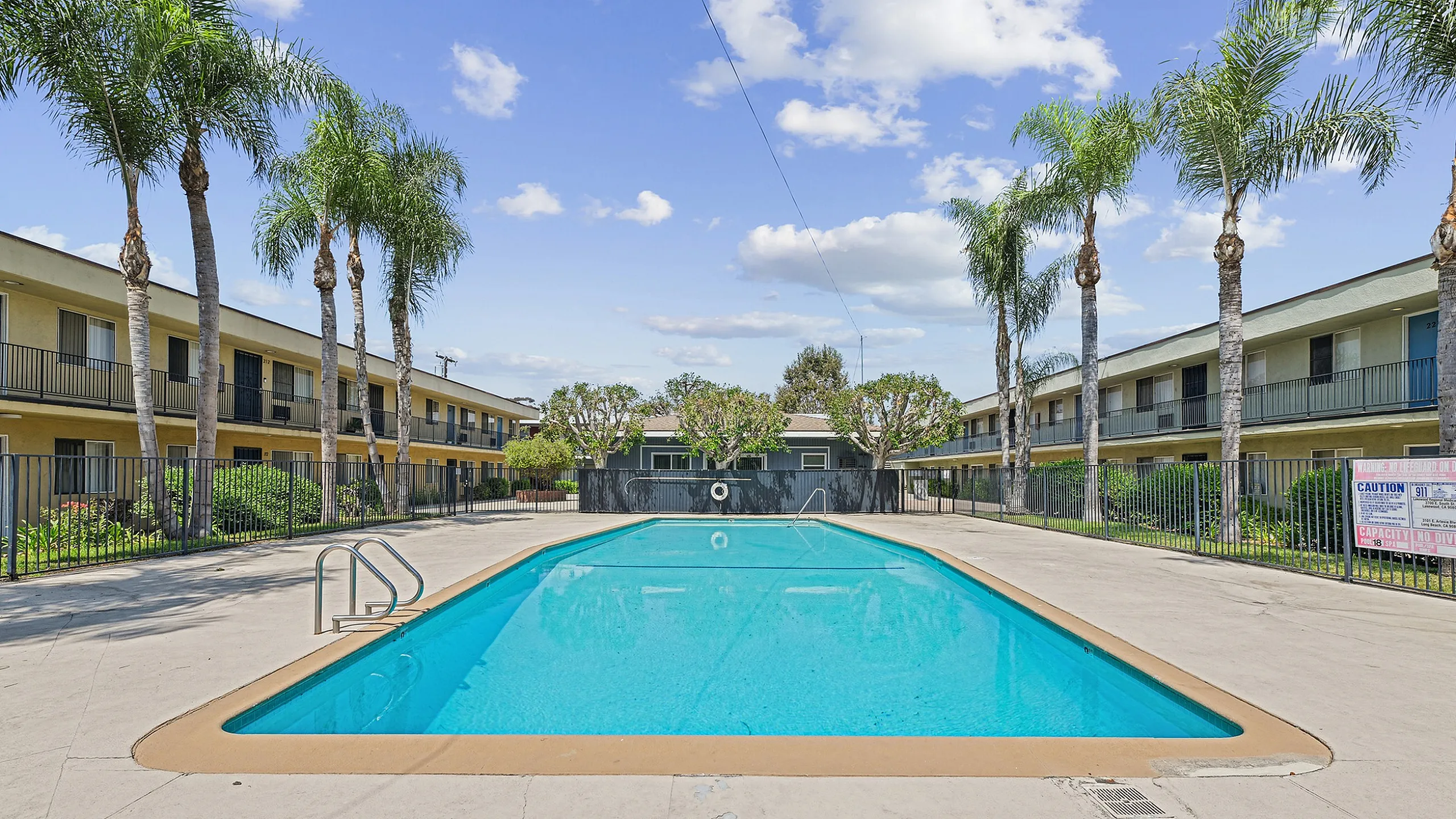 Inviting outdoor pool surrounded by lush palm trees and modern apartment complex, offering a relaxing oasis under a bright blue sky.