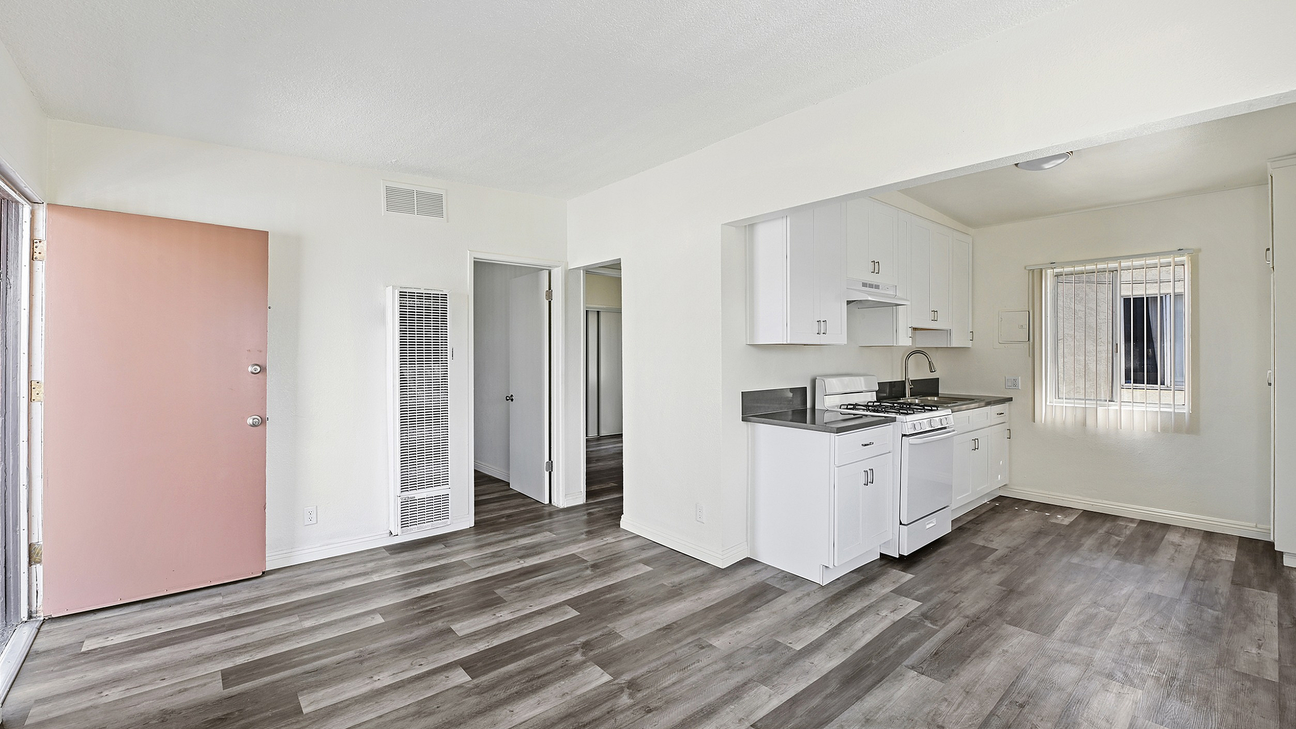 Bright and inviting open-plan kitchen and living area featuring sleek white cabinets and modern appliances, complemented by stylish wood flooring.