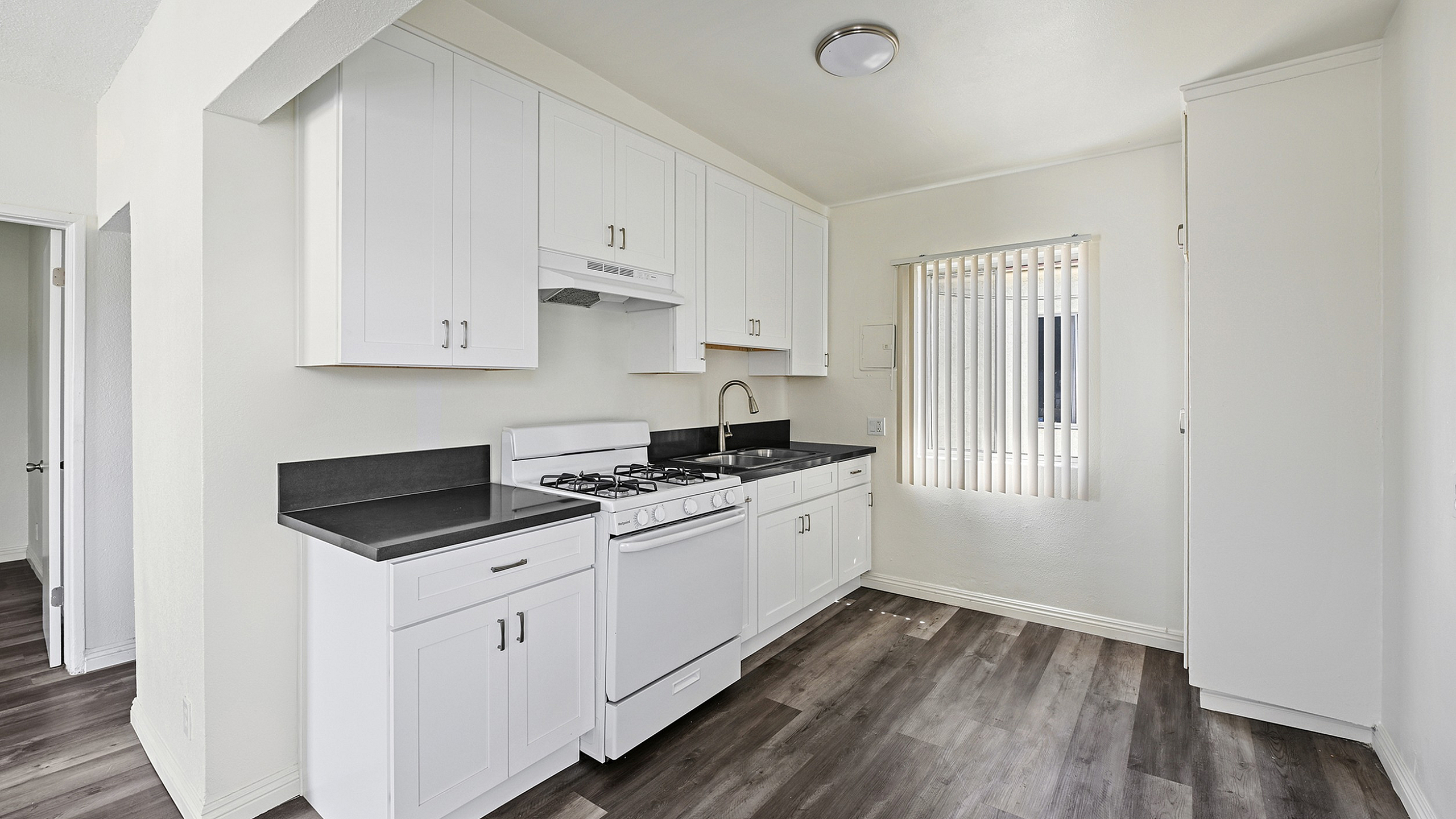 Bright, modern kitchen featuring sleek white cabinetry, stylish black countertops, and elegant wood flooring.