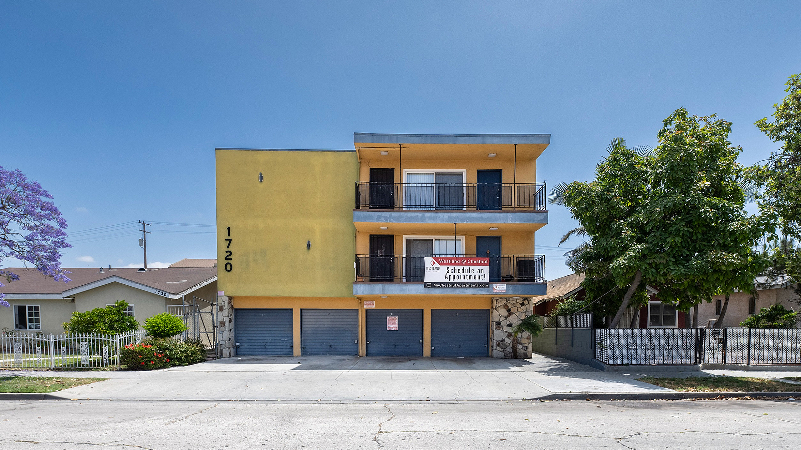 Contemporary apartment building with vibrant yellow facade, featuring spacious balconies and lush greenery, ideal for modern living.
