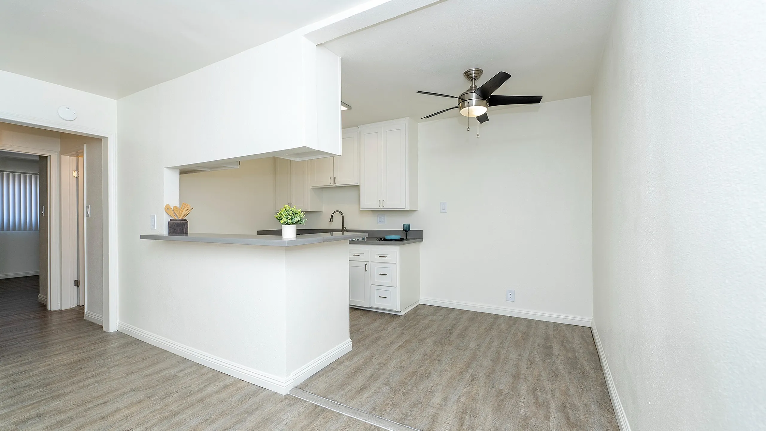 Bright and modern open-floor kitchen with sleek white cabinets, stylish ceiling fan, and elegant wooden flooring.