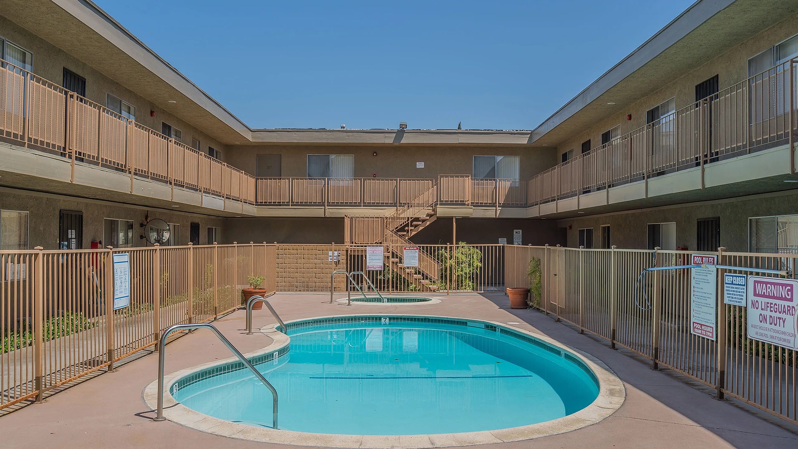 Inviting courtyard with a refreshing swimming pool, surrounded by charming two-story apartment balconies under a clear blue sky.