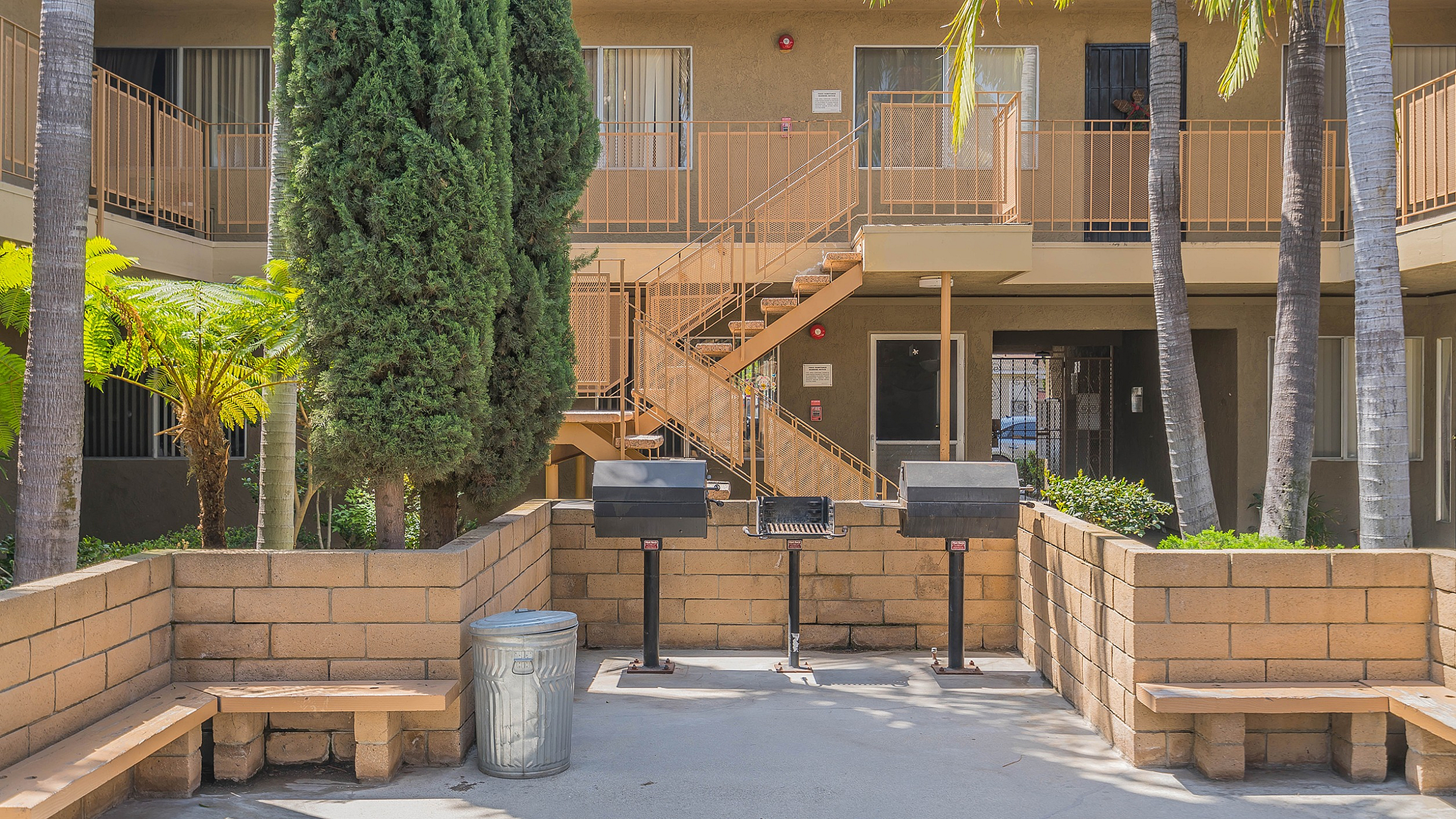 Charming apartment courtyard featuring lush greenery, modern barbecue grills, and inviting outdoor seating areas.