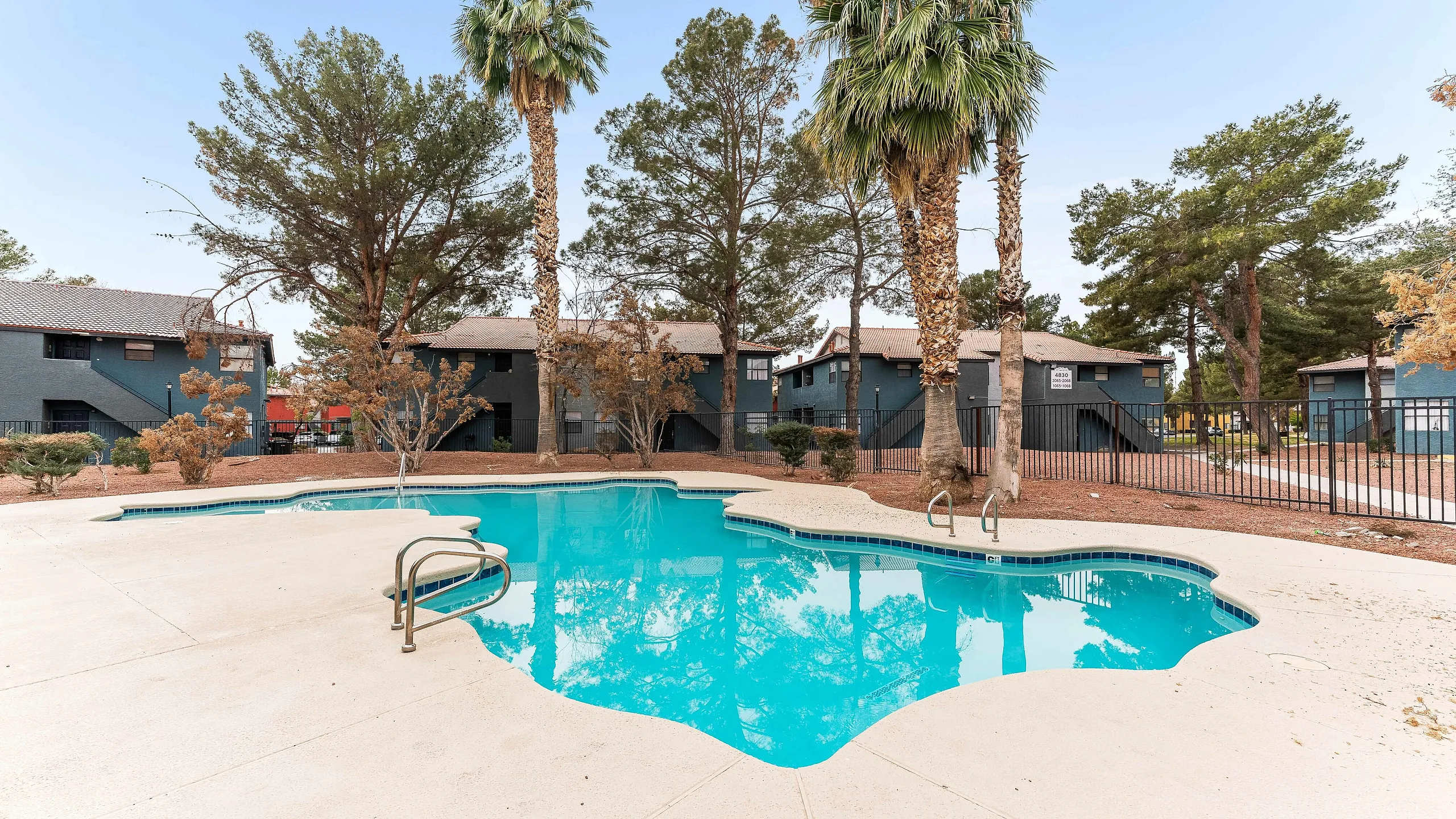 Inviting apartment complex with a refreshing pool, surrounded by palm trees and lush greenery, perfect for relaxing in a serene setting.