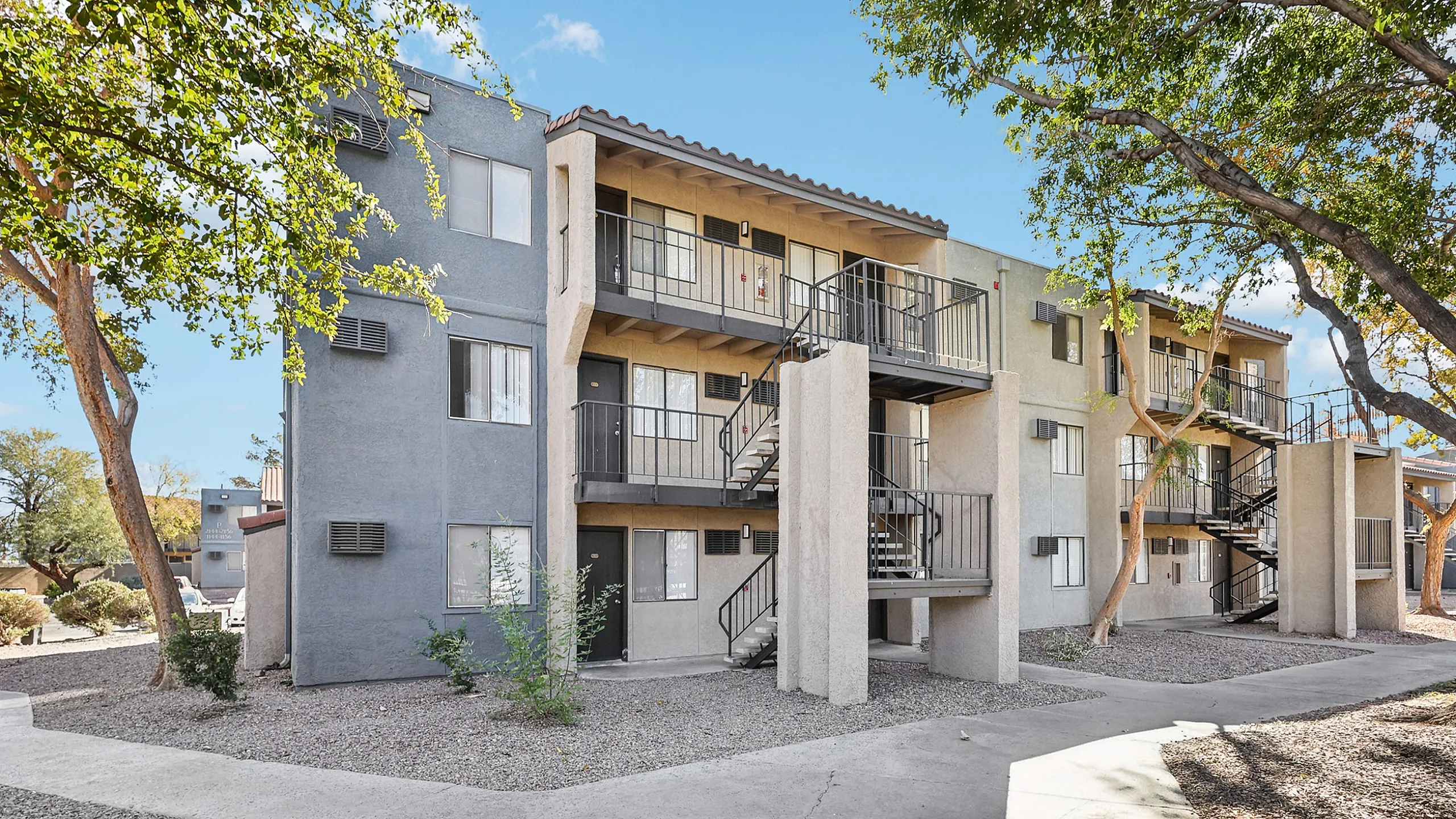 Modern apartment complex with lush greenery, featuring stylish balconies and contemporary design under a clear blue sky.