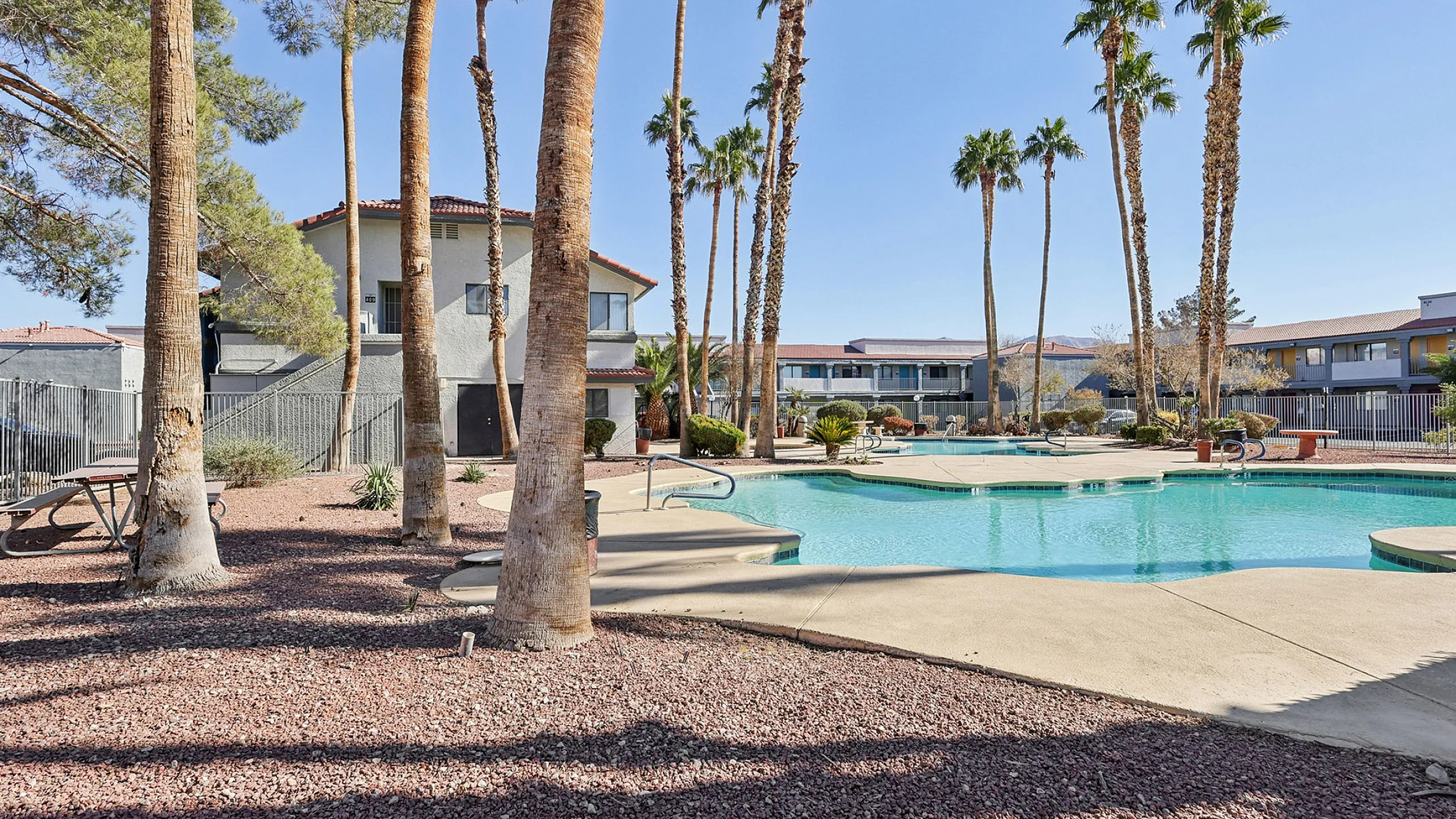 Inviting apartment complex with a serene pool area surrounded by tall palm trees and landscaped grounds, perfect for relaxation.
