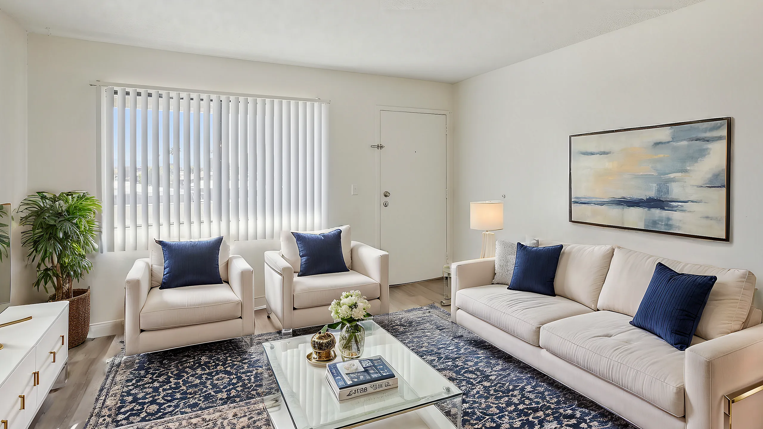 Bright and inviting living room with elegant white furniture, plush navy accents, and a modern glass coffee table, perfect for relaxation and entertainment.