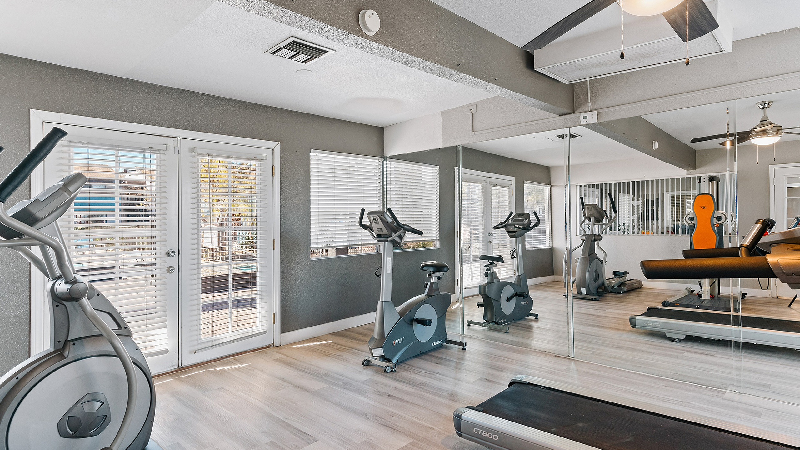 Chic and bright fitness room featuring modern exercise equipment and mirrored walls with natural light streaming through large windows.