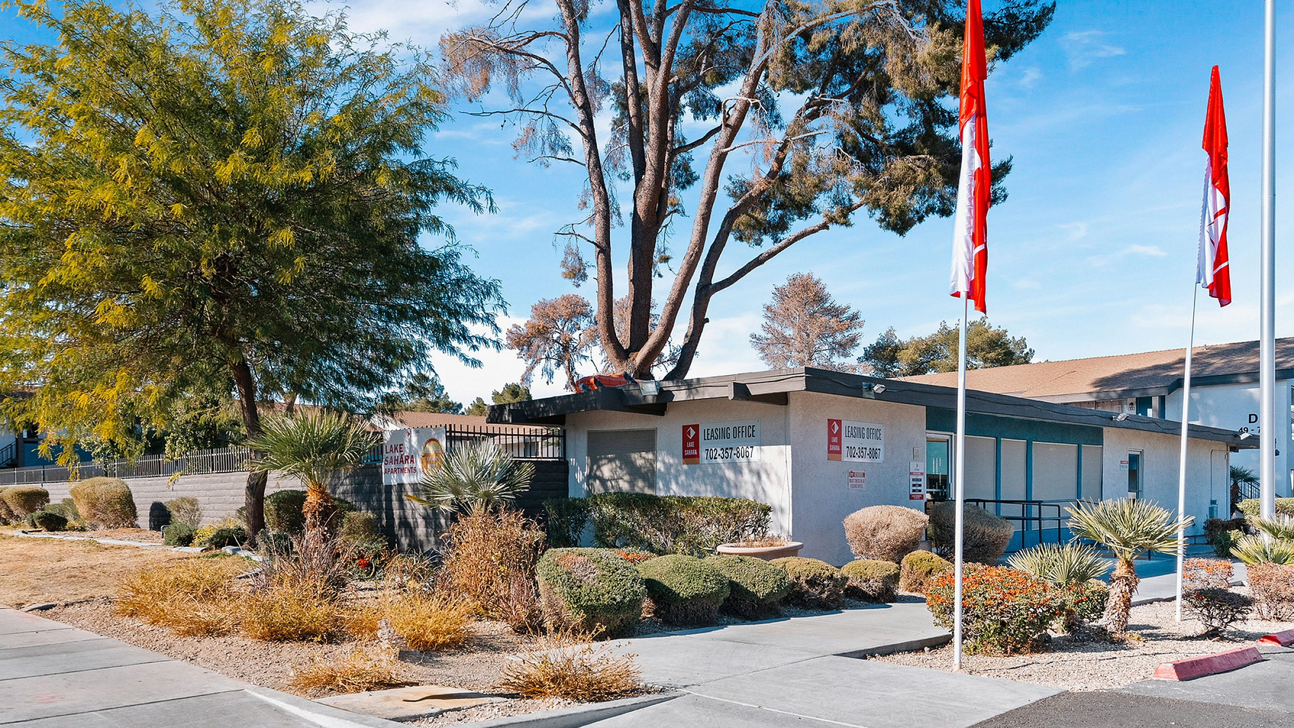 Inviting leasing office of Lake Sahara Apartments surrounded by lush green landscaping and vibrant flags, epitomizing a welcoming community atmosphere.