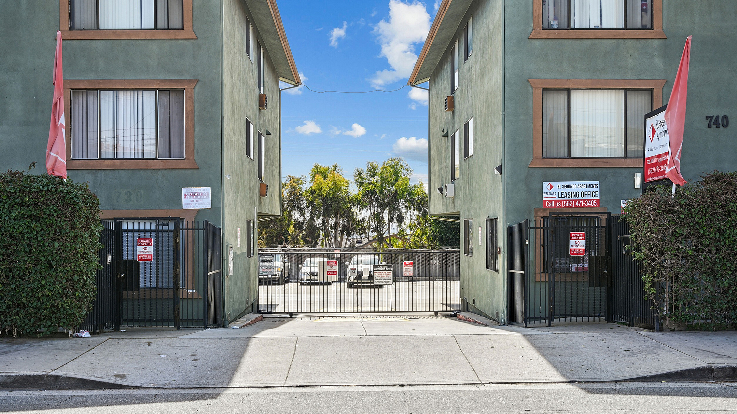 Inviting apartment entrance with lush greenery and secure gated access, offering modern living spaces.