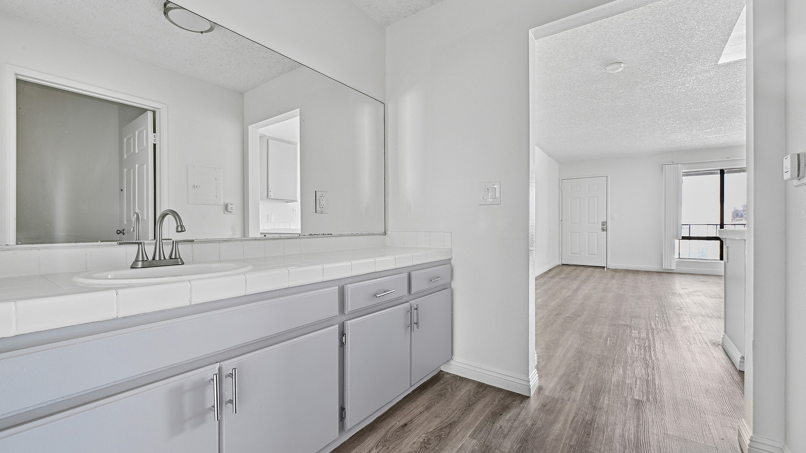 Bright, modern apartment interior with elegant vanity, light cabinetry, and sleek wood floors leading to a spacious living area.