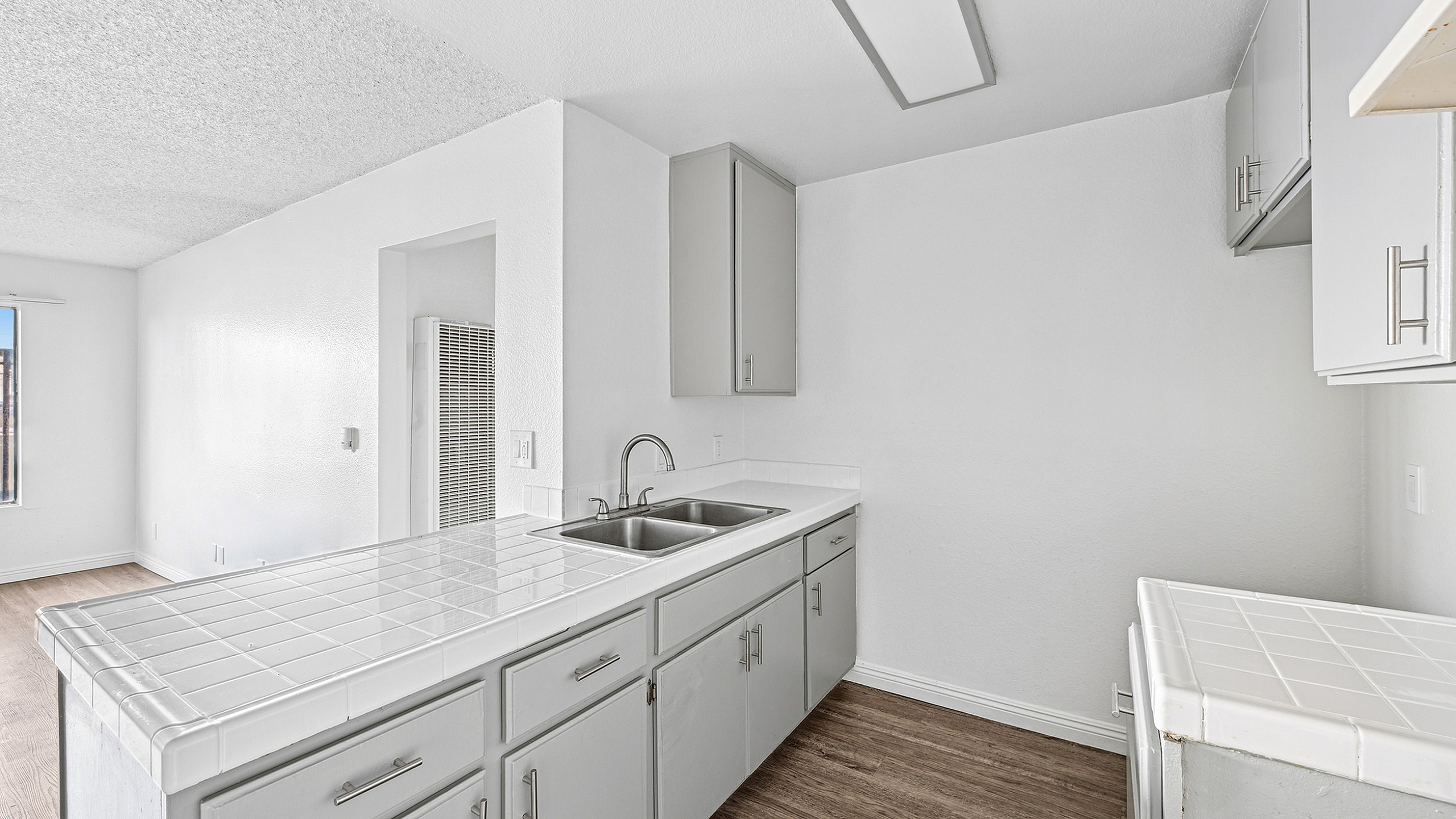 Bright and inviting kitchen with modern cabinetry and elegant tile countertops, seamlessly adjoining a cozy living area with natural light streaming through large windows.