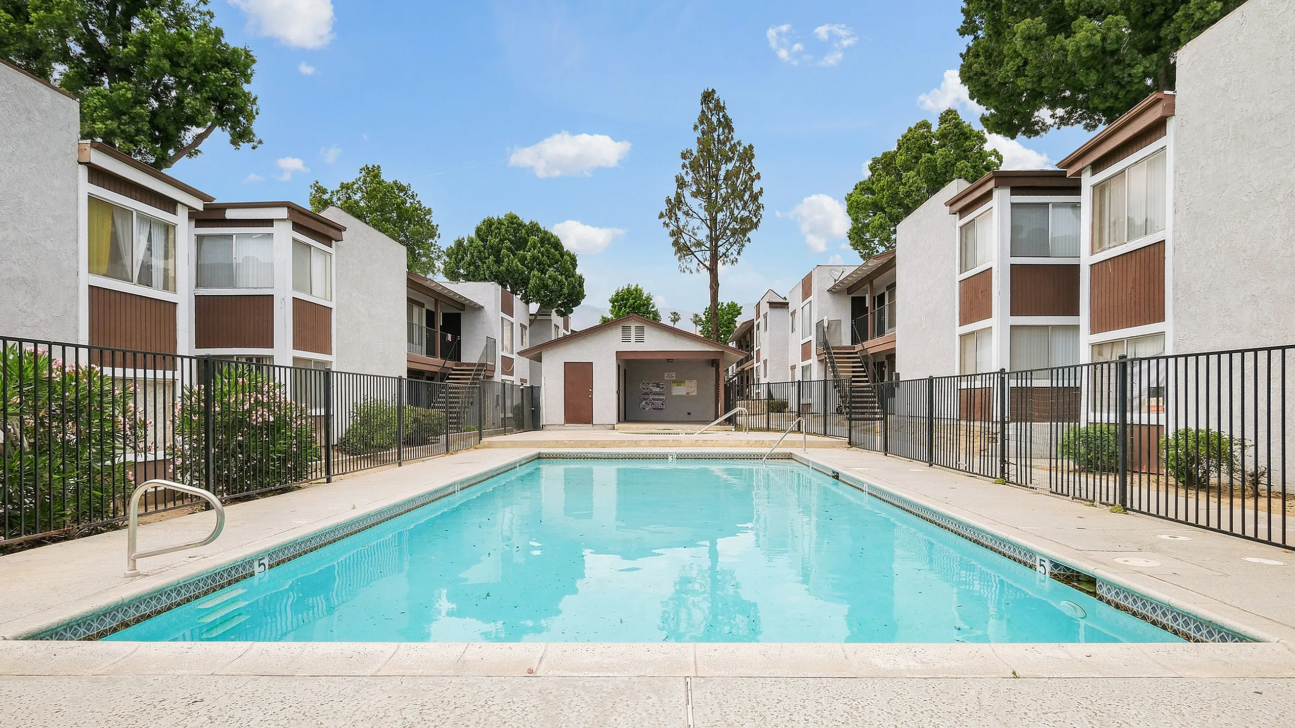 Inviting apartment complex featuring a sparkling swimming pool surrounded by lush green trees and modern buildings, perfect for relaxation and leisure.