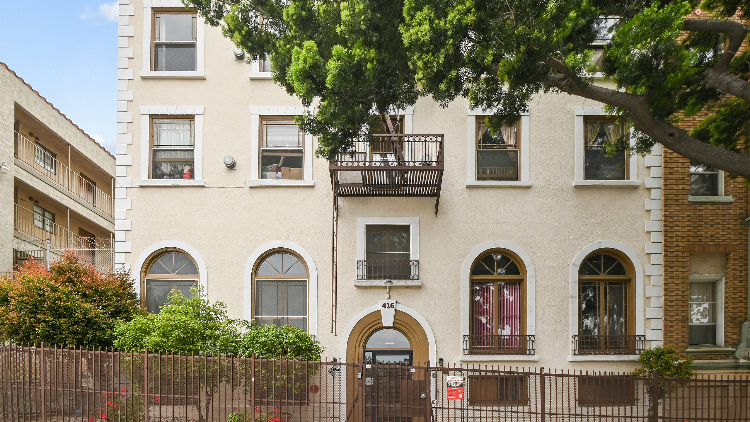 Charming apartment building with classic architecture, featuring arched windows, a small balcony, and lush surrounding trees.