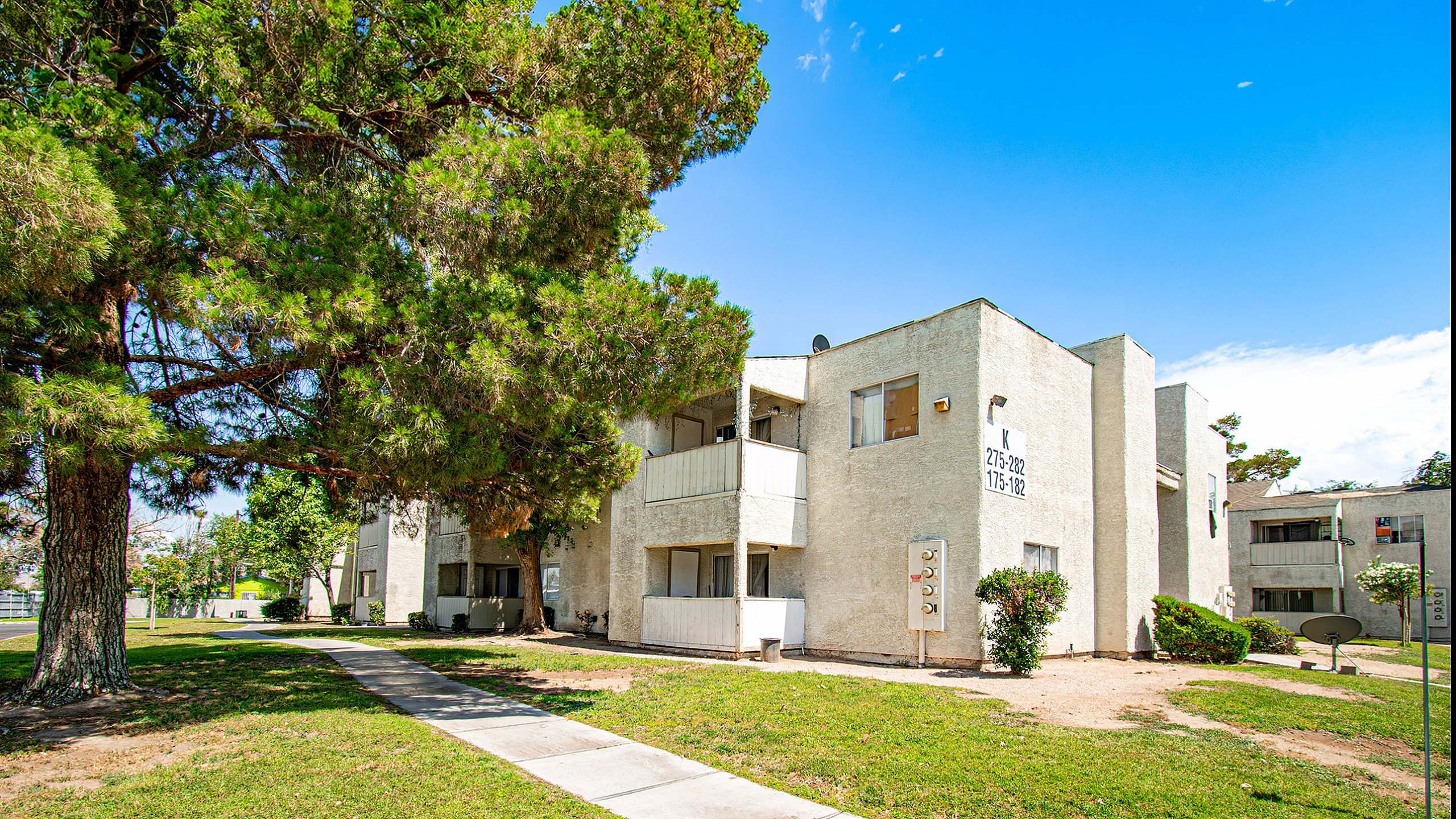 Charming two-story apartment building with spacious balconies and lush green surroundings, perfect for a serene lifestyle.