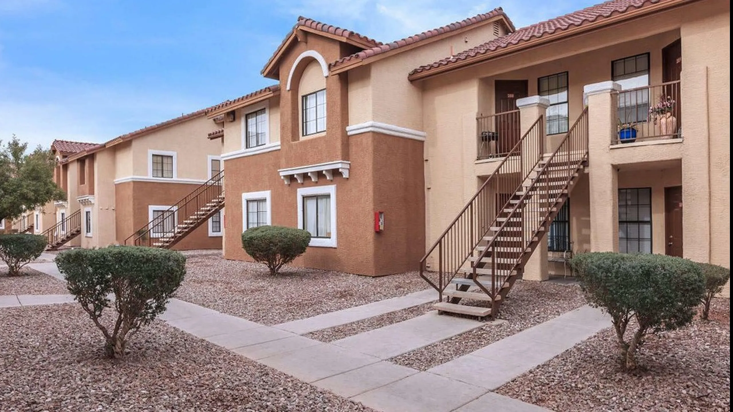 Charming two-story apartment complex with inviting outdoor staircases and well-maintained landscaping under a clear blue sky.