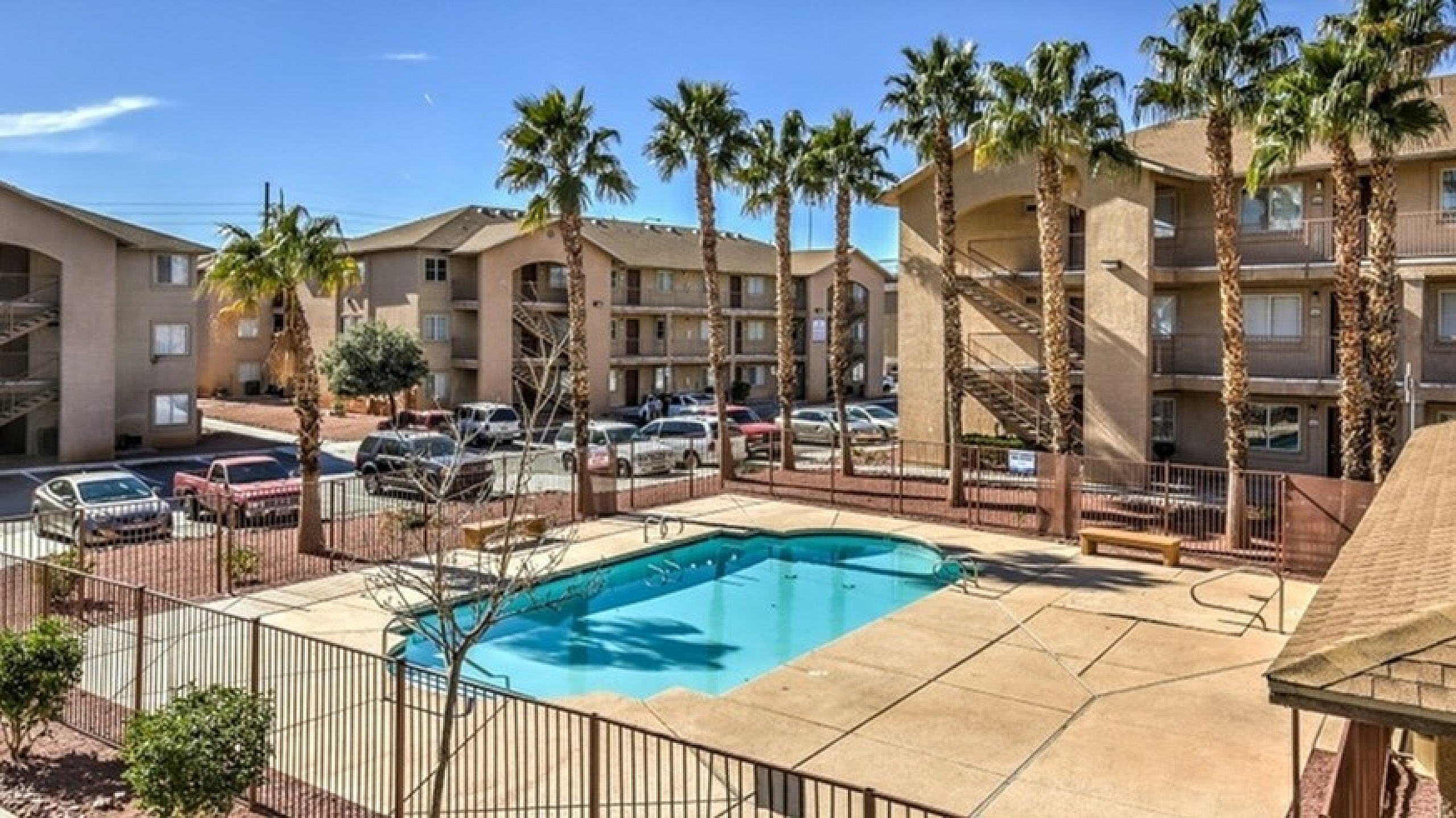 Charming apartment complex with inviting swimming pool, surrounded by palm trees and sunlit buildings, offering a relaxing and vibrant living experience.