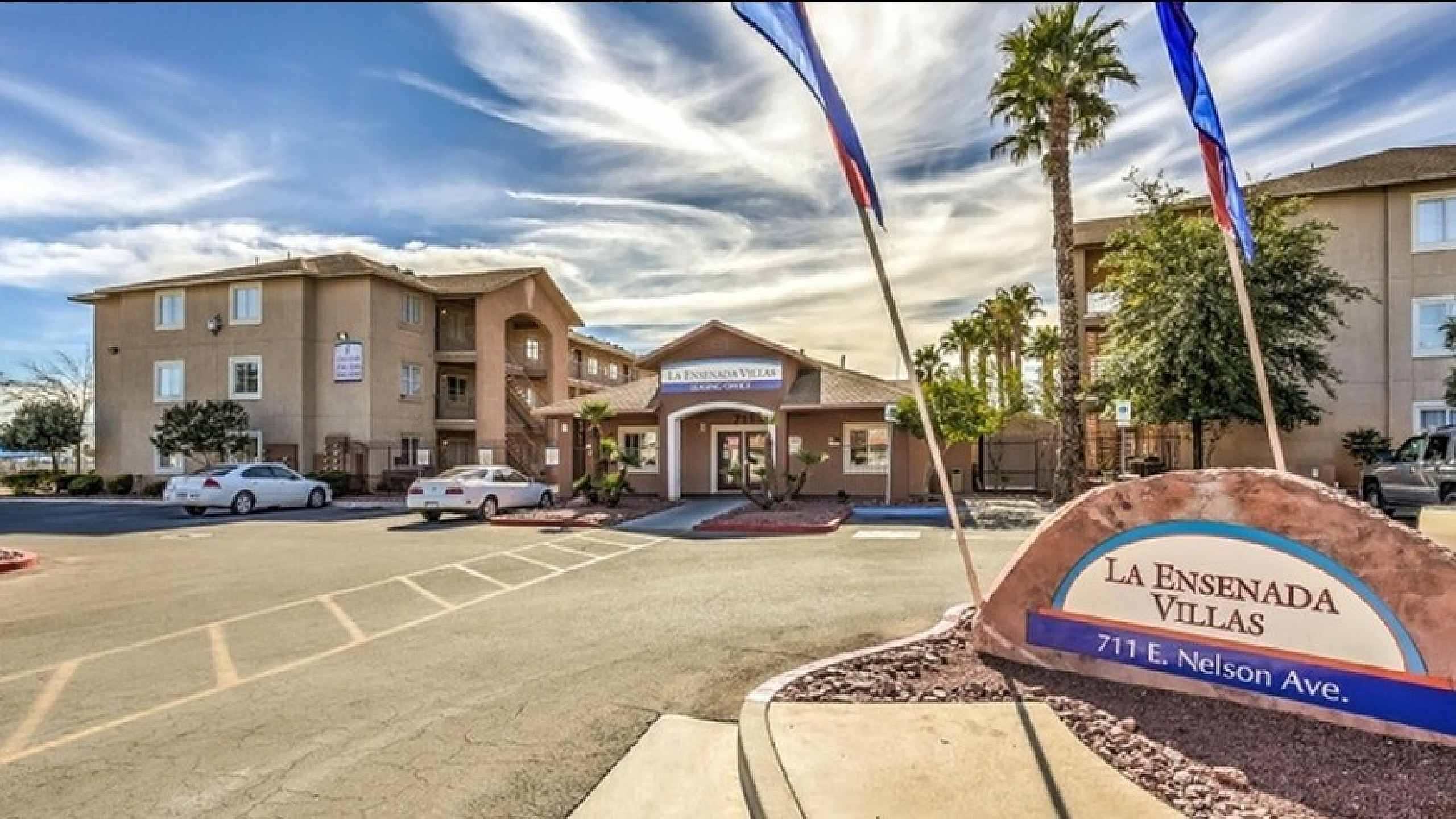 Welcoming entrance to La Ensenada Villas with vibrant landscaping and ample parking, showcasing a serene apartment community.