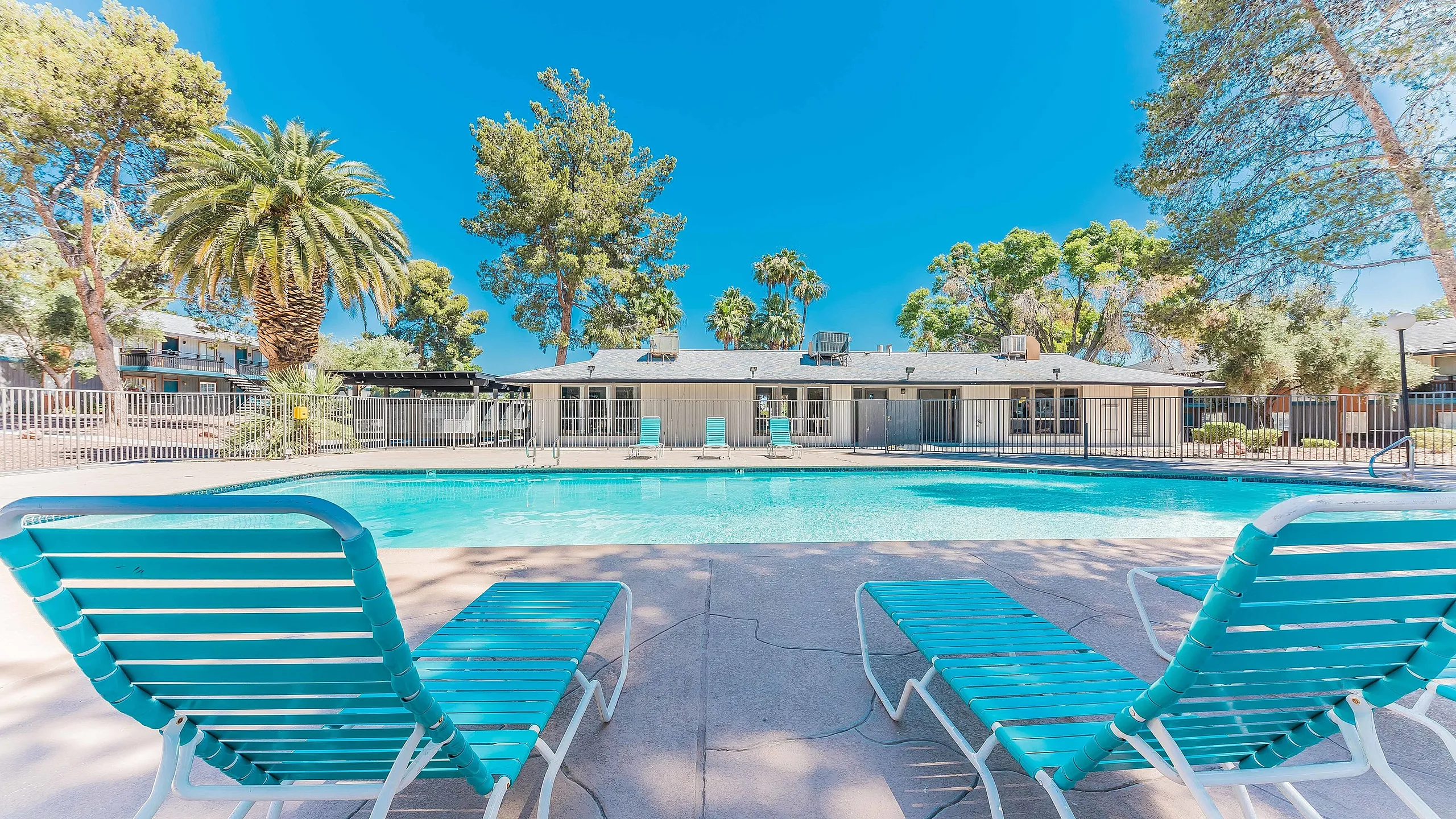 Inviting outdoor pool area with vibrant turquoise loungers, surrounded by lush palm trees and bright blue skies, offering a serene retreat.