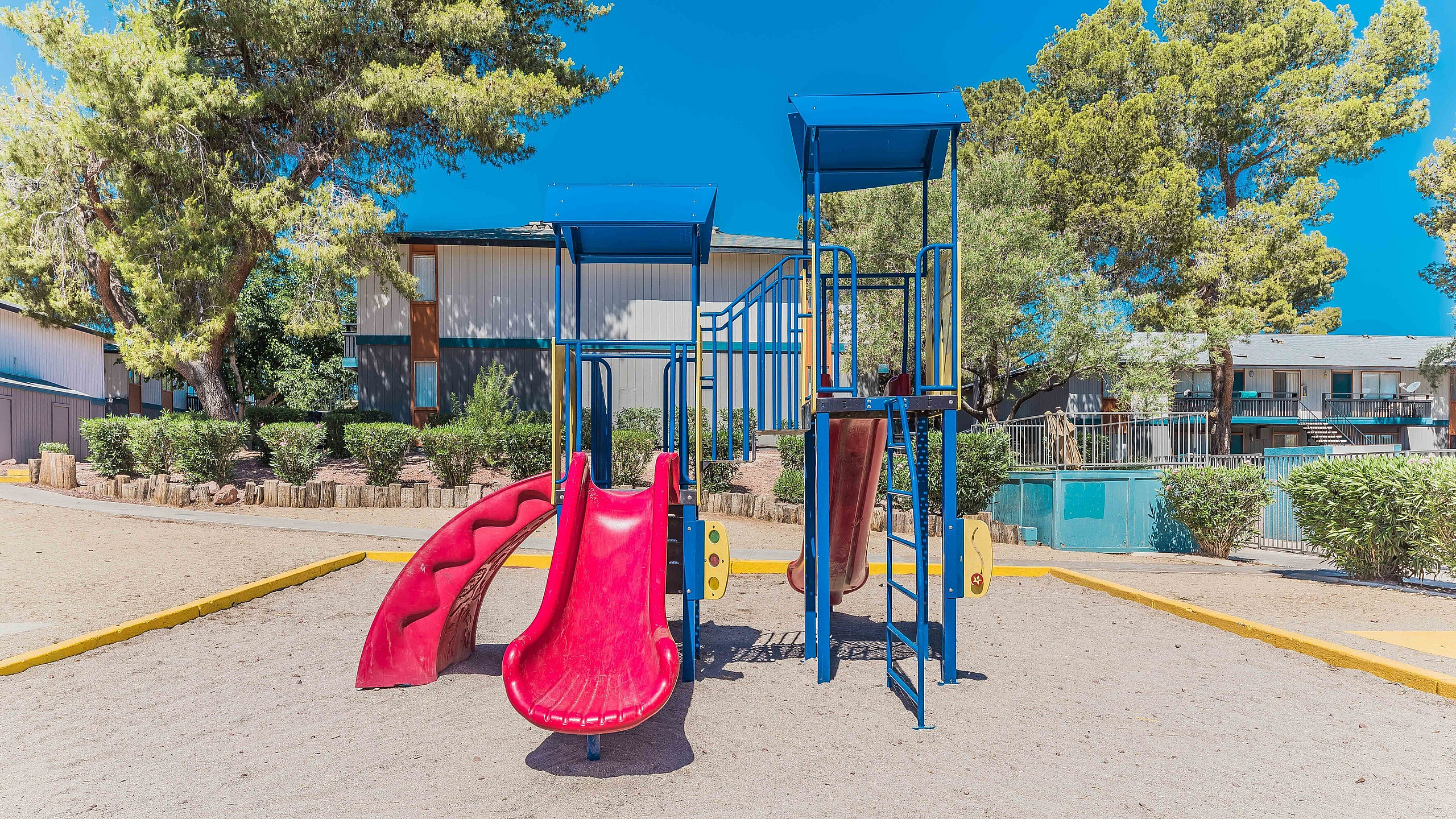 Inviting playground area featuring vibrant slides, surrounded by lush greenery and well-maintained apartment buildings.