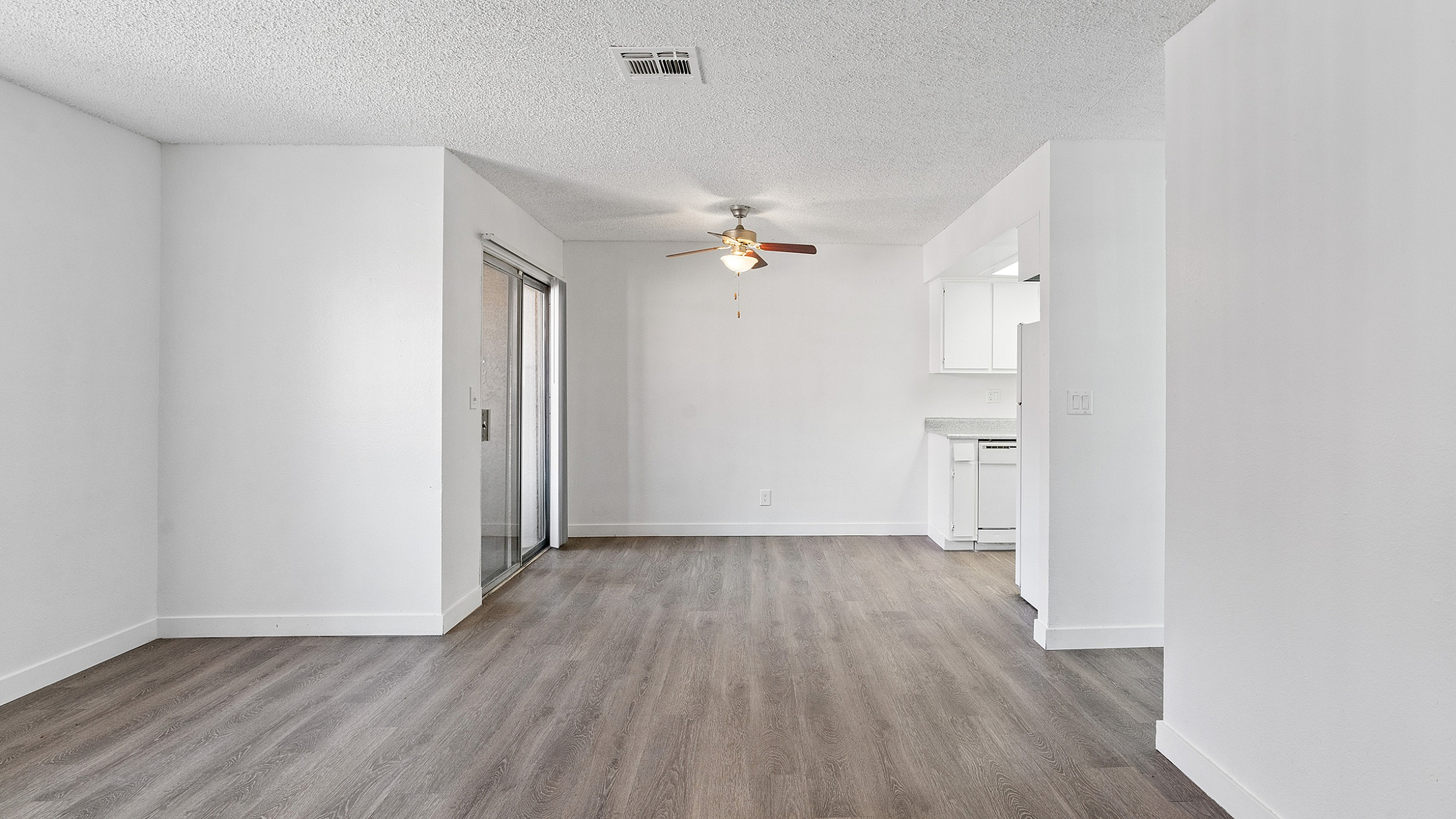Bright and modern living area with elegant wood flooring, ceiling fan, and stylish open-concept kitchen, perfect for contemporary living.