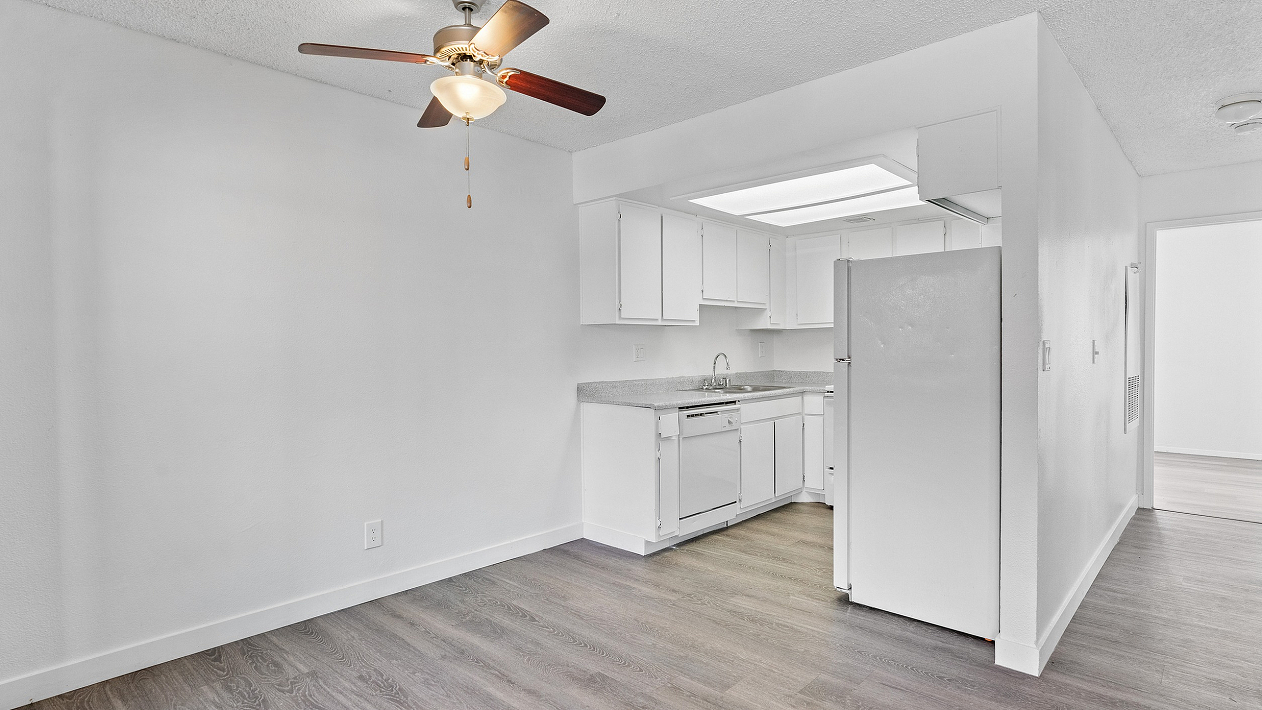 Bright and airy apartment kitchen with sleek white cabinetry, modern appliances, and elegant hardwood flooring under a stylish ceiling fan.