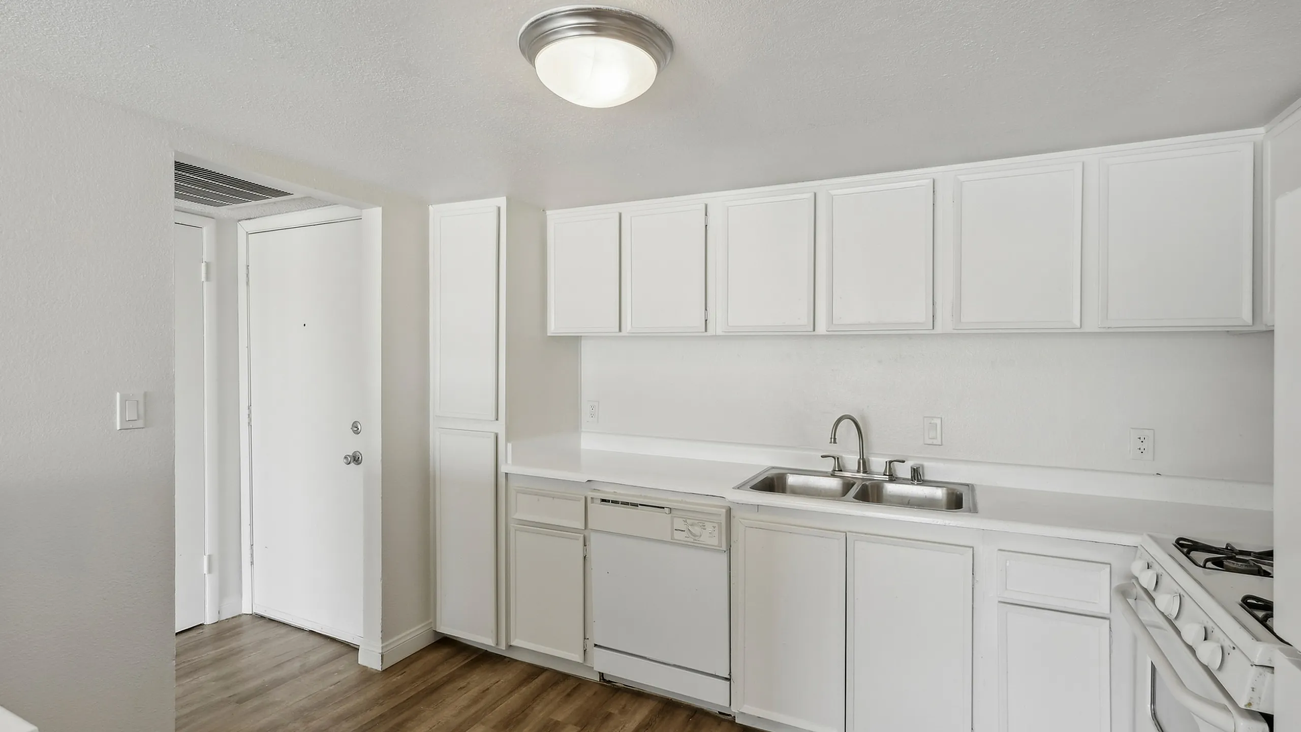 Bright and modern kitchen with sleek white cabinets, stainless steel sink, and elegant wooden flooring.