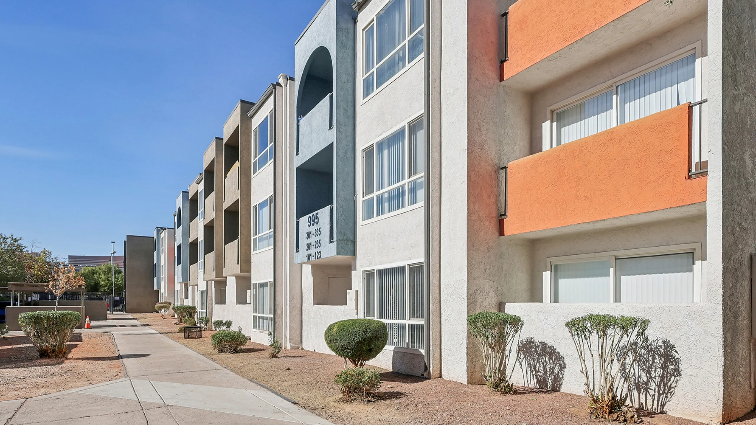 Modern apartment complex with vibrant colored exteriors, featuring well-maintained walkways and lush greenery under a clear blue sky.