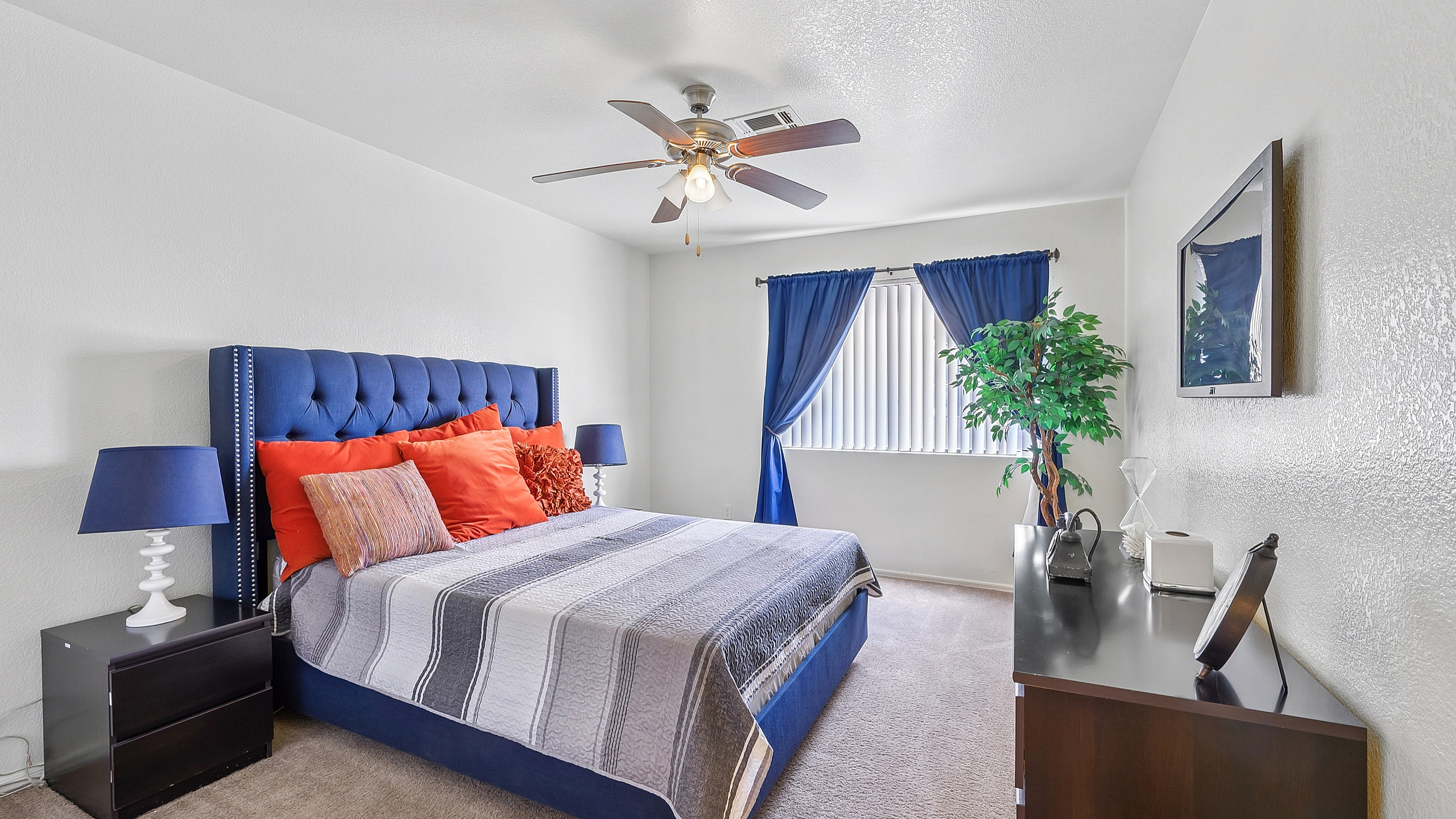 Bright and cozy bedroom featuring a plush blue bed with vibrant red pillows, elegant nightstands with matching blue lamps, and a window adorned with stylish blue curtains.