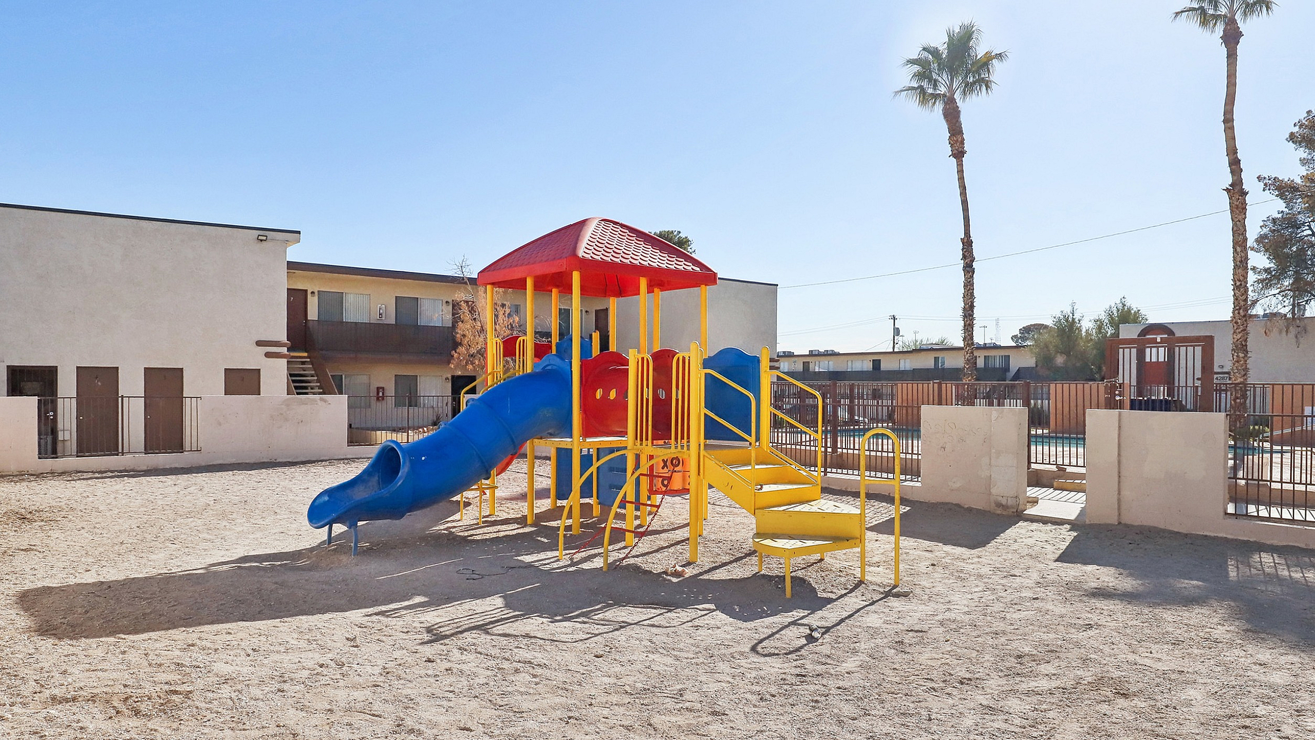 Vibrant playground with a colorful slide and climbing structure, perfect for family-friendly living in a sunny apartment community.