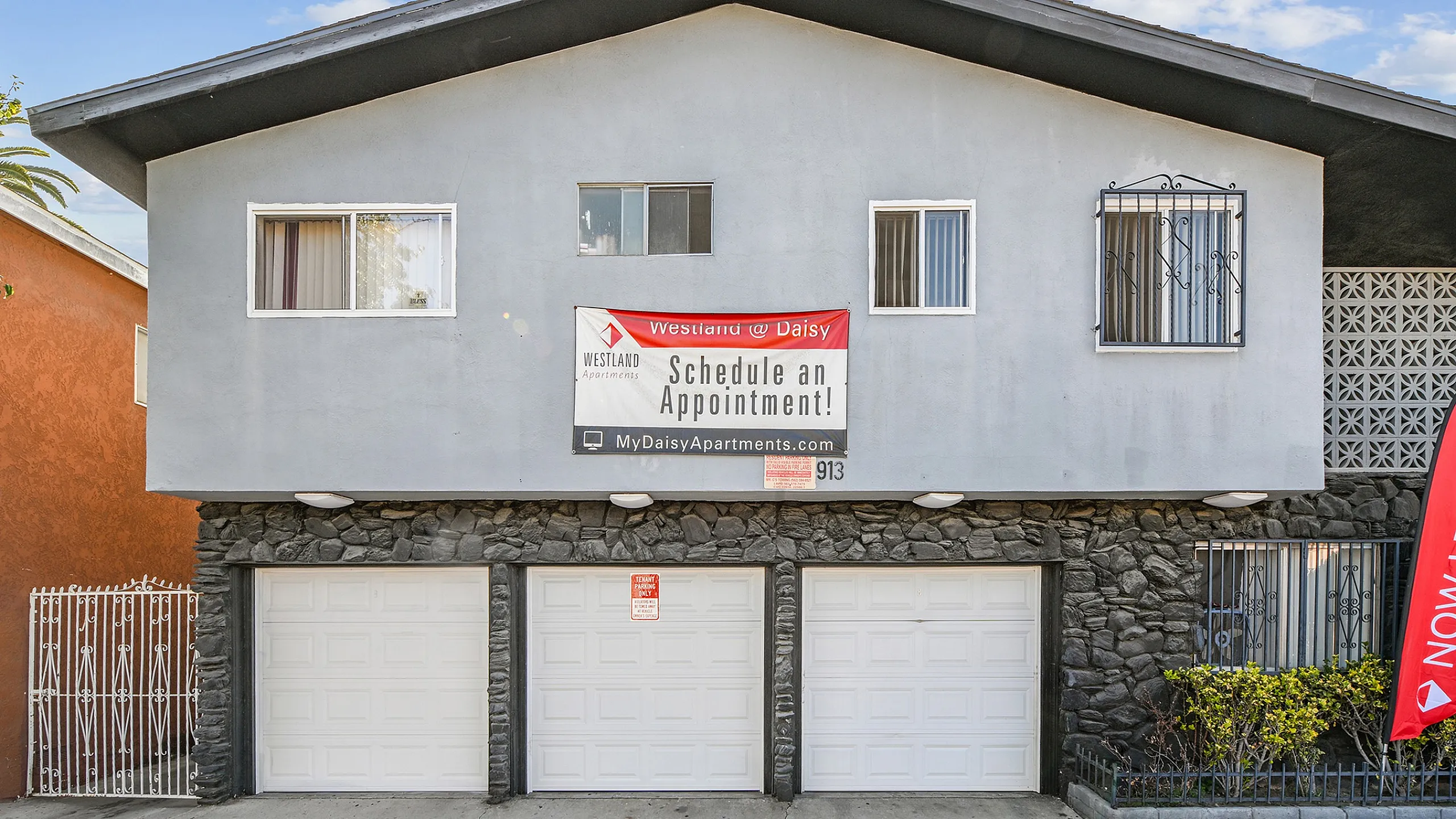 Charming apartment exterior with modern design, featuring a prominent schedule appointment banner and convenient garage access under a clear blue sky.