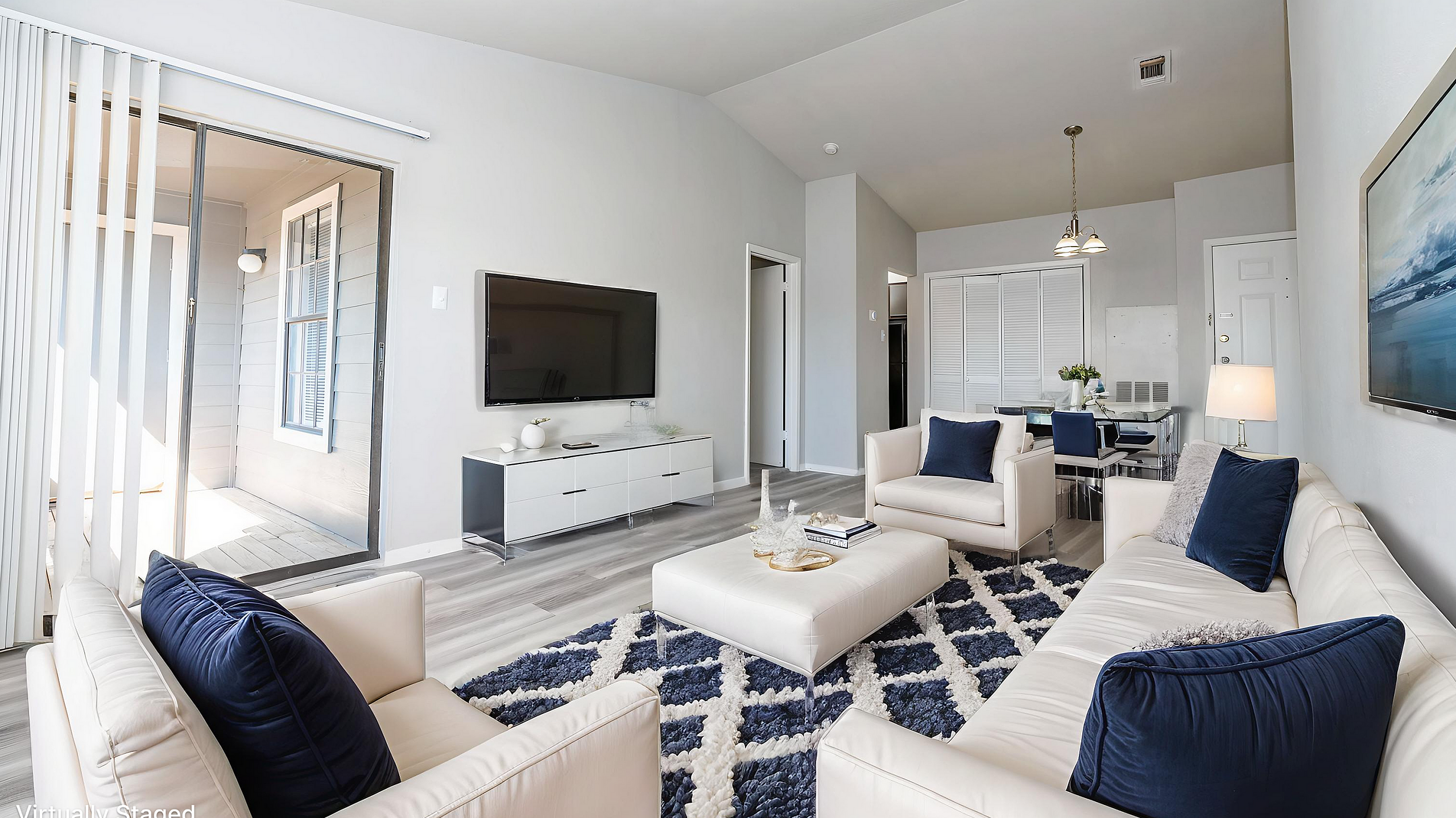 Modern, virtually staged living room with elegant white sofas, plush blue cushions, and a chic TV setup, opening to a sunlit patio.