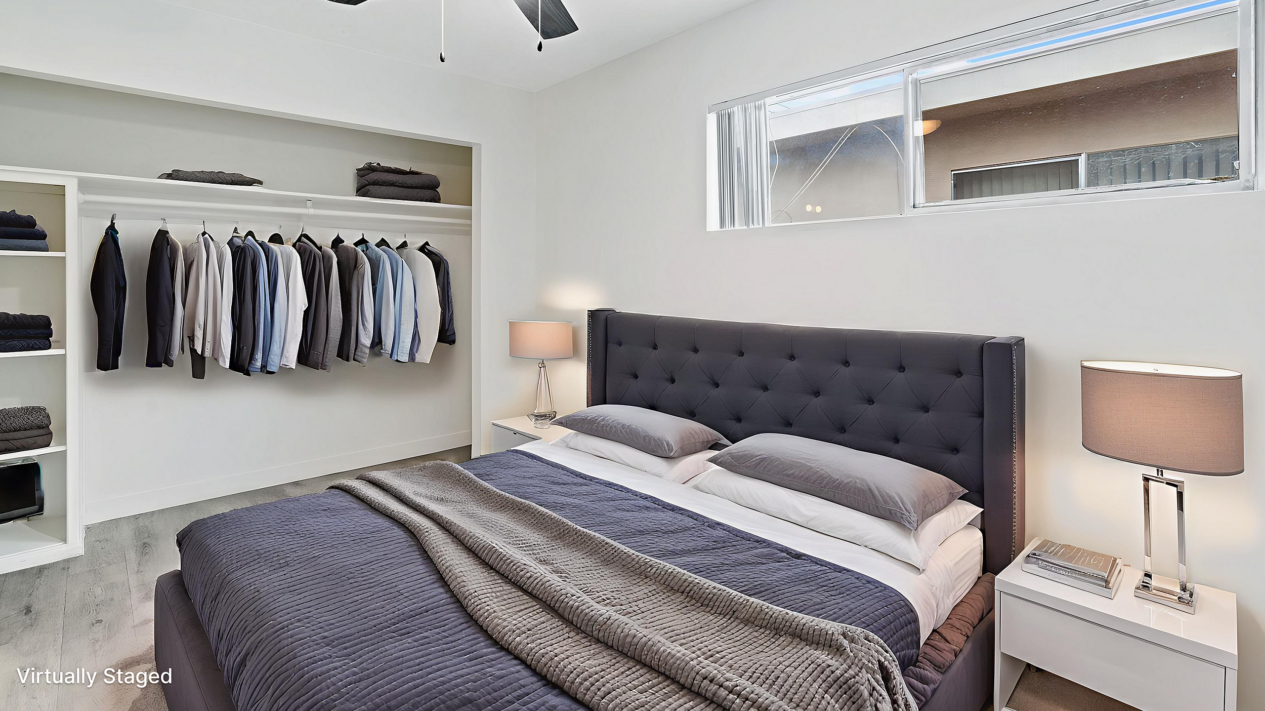 Sleek and modern virtually staged bedroom featuring a cozy bed with elegant gray linens, a stylish ceiling fan, and a smart wardrobe display.