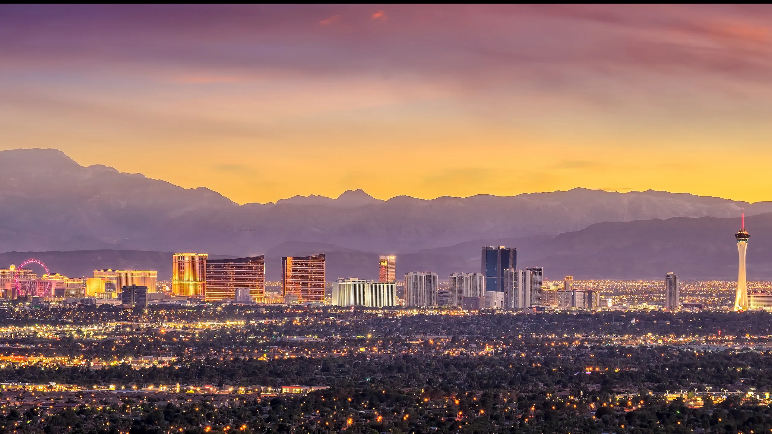Breathtaking panoramic view of a vibrant cityscape at sunset, showcasing illuminated skyscrapers, iconic landmarks, and a serene mountain backdrop.