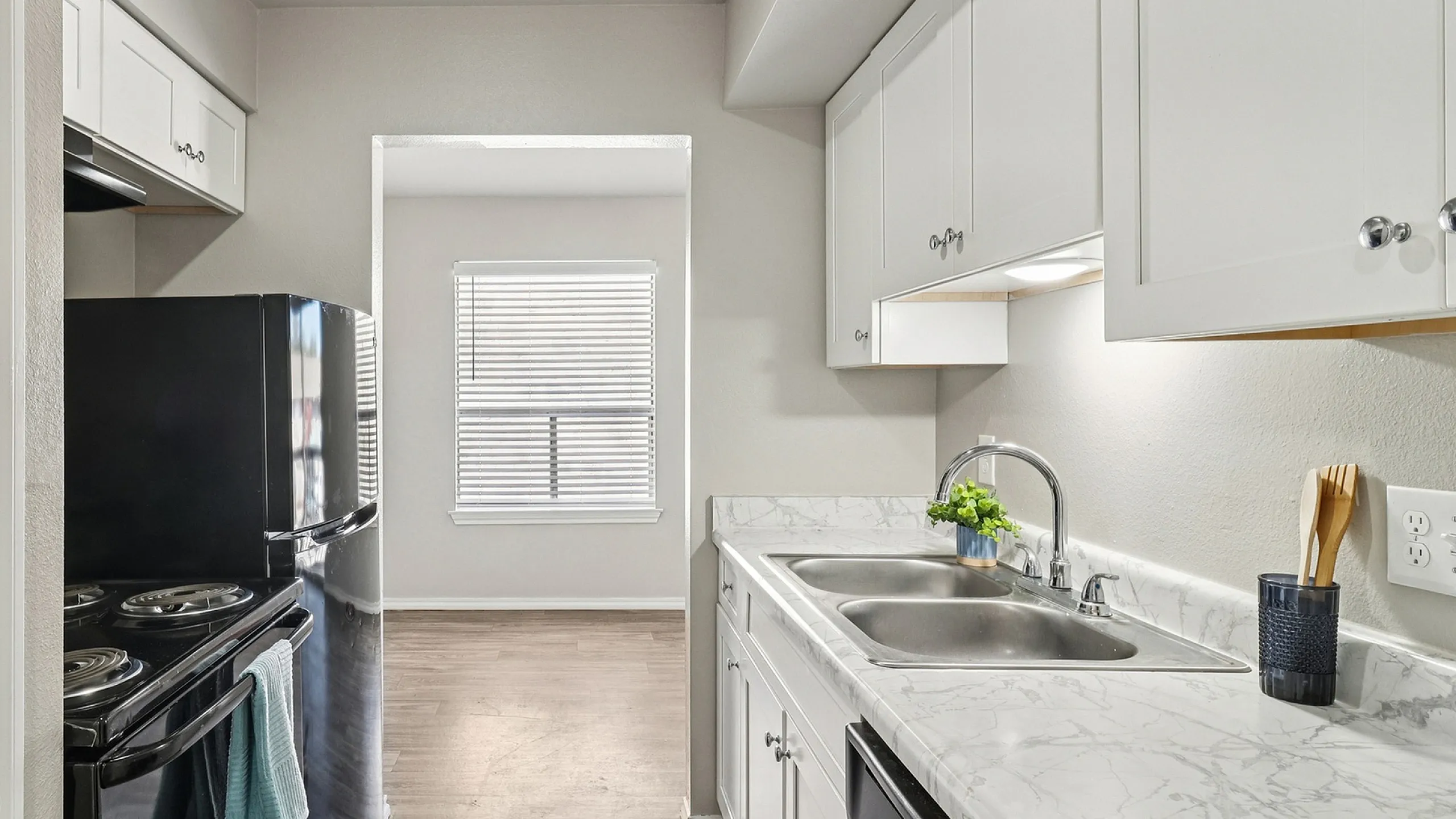 Modern kitchen boasting sleek black appliances, elegant marble countertops, and ample natural light from a large window.