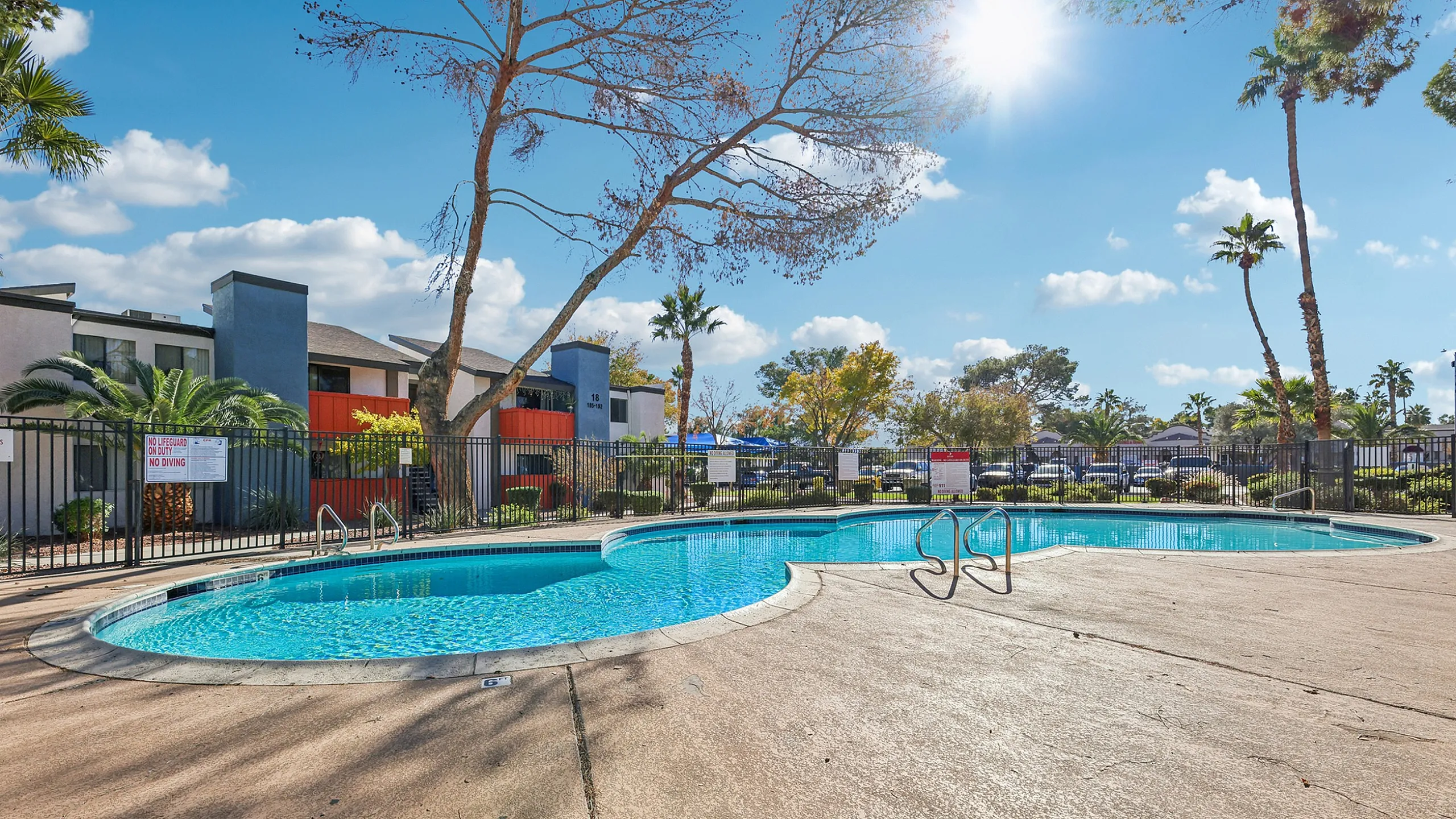 Inviting outdoor pool area with crystal clear water, surrounded by scenic palm trees and modern apartments, under a bright blue sky.