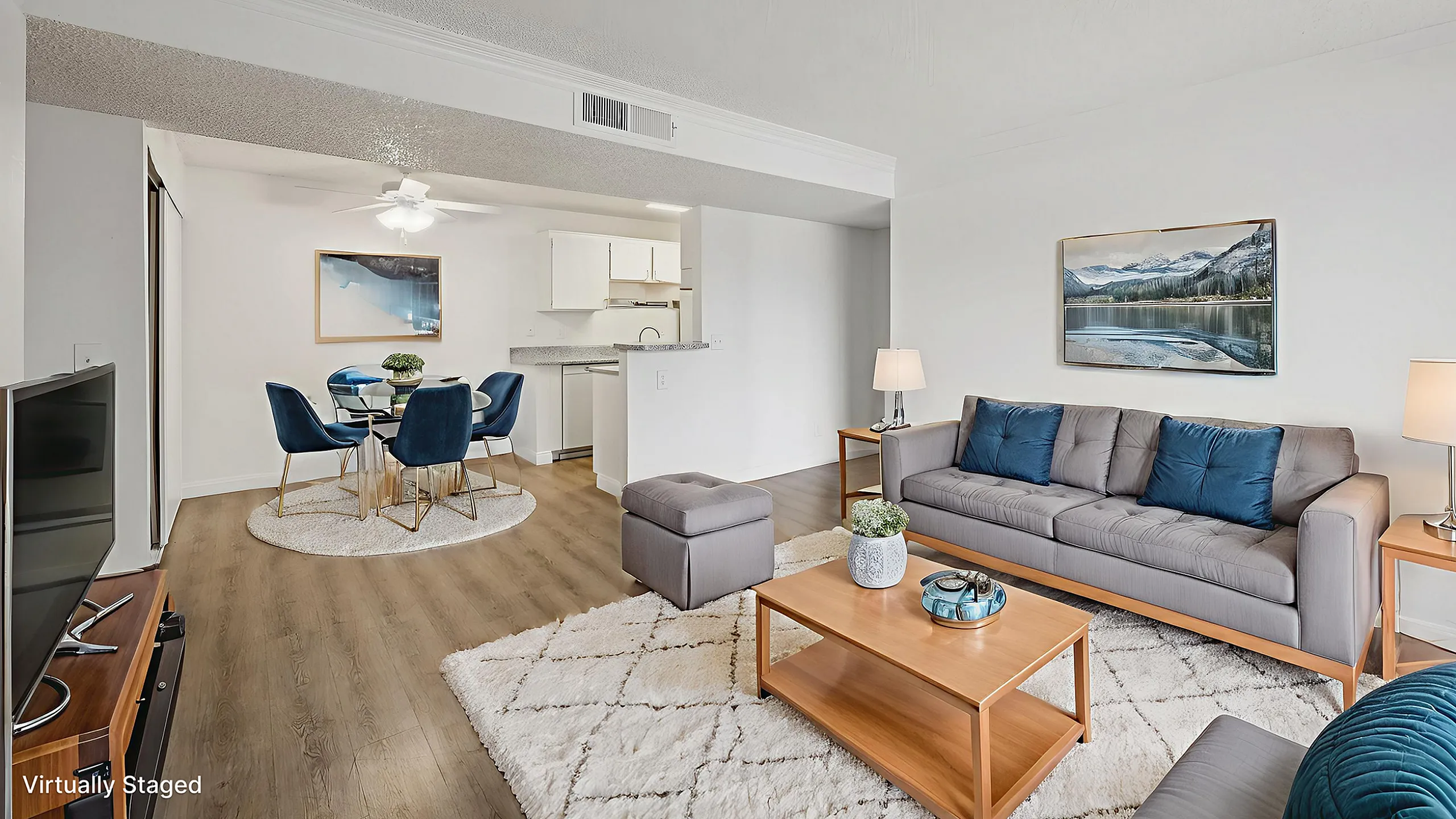 Virtually staged modern apartment living room with plush gray sofa, stylish coffee table, cozy area rug, and open layout leading to a chic dining area with elegant blue chairs and a sleek kitchen.