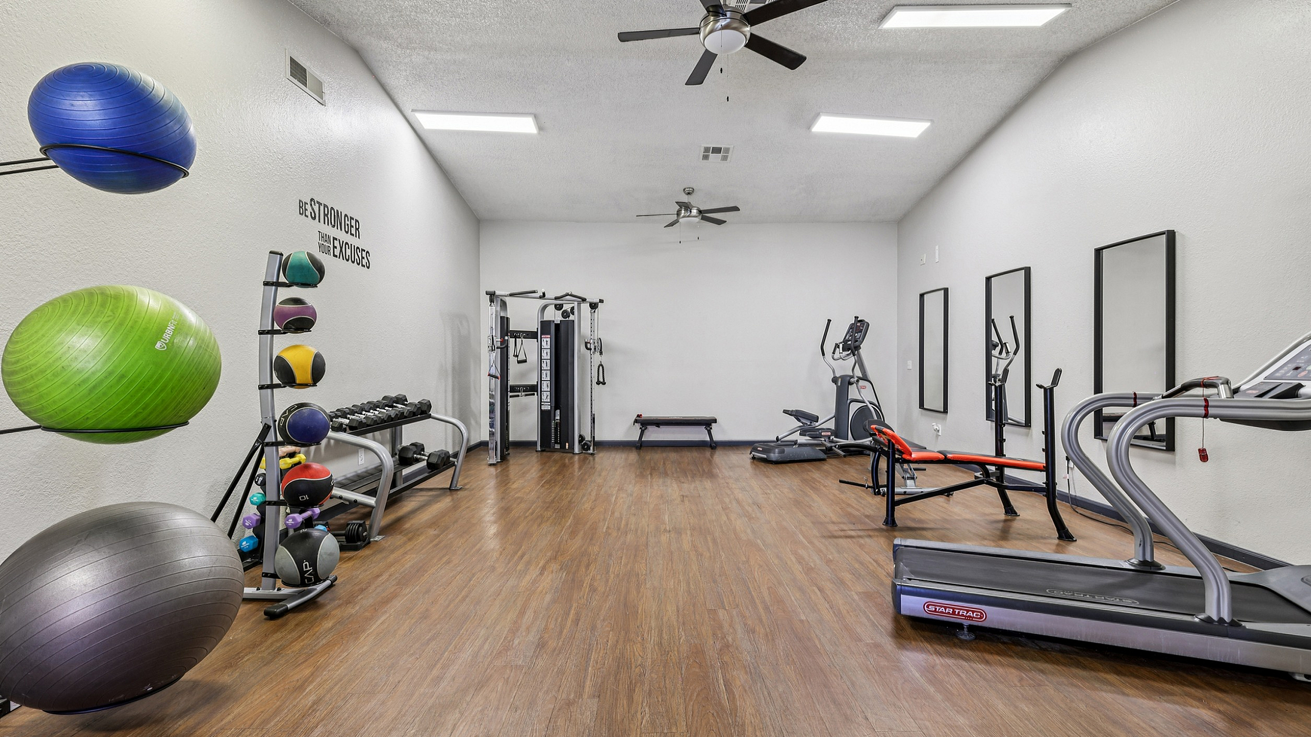Inviting fitness center with state-of-the-art gym equipment, motivational decor, and a polished wooden floor for an energetic workout experience.