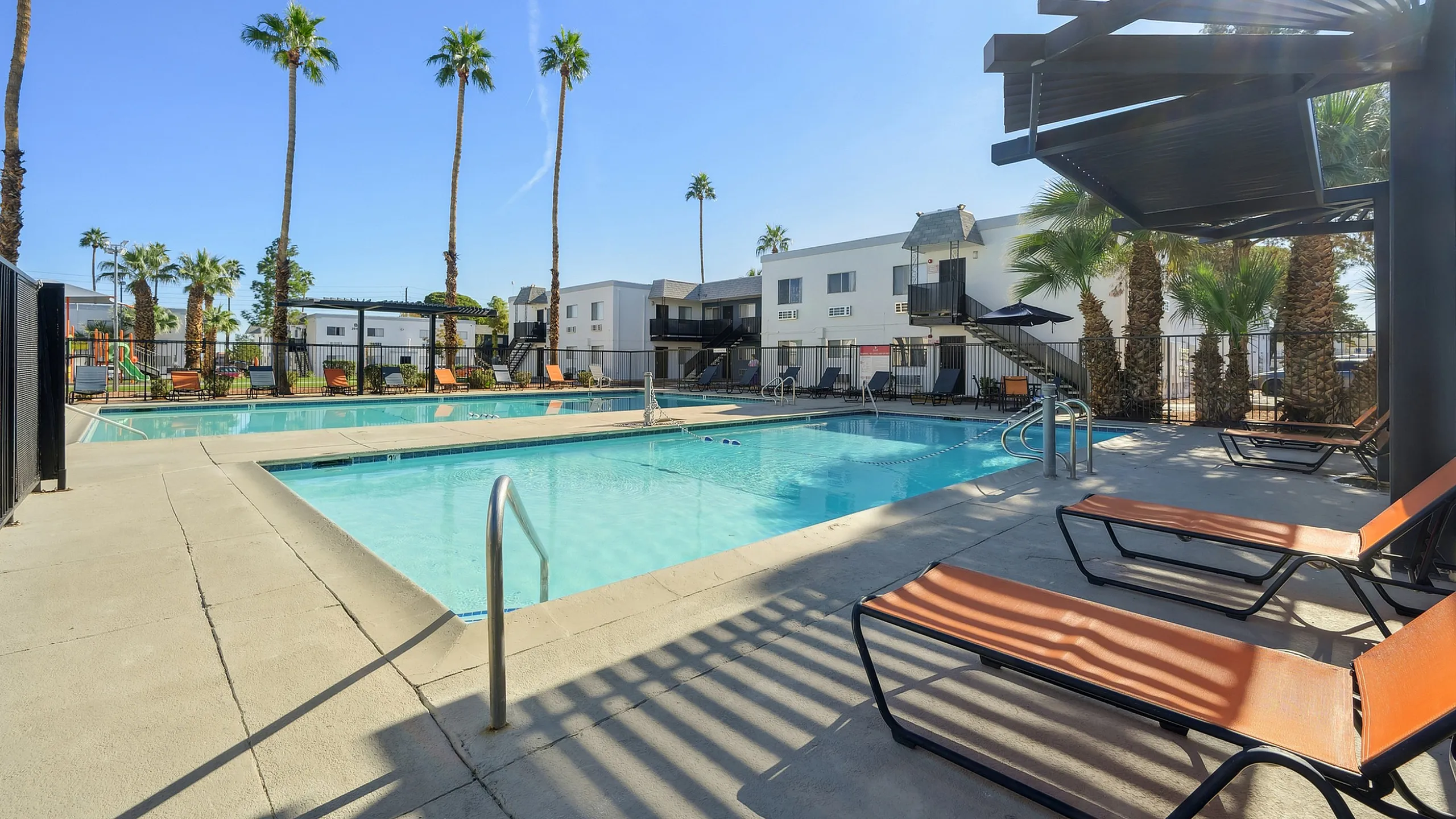 Luxurious apartment complex featuring a sparkling pool surrounded by tropical palm trees and modern lounge chairs, ideal for relaxation and leisure.