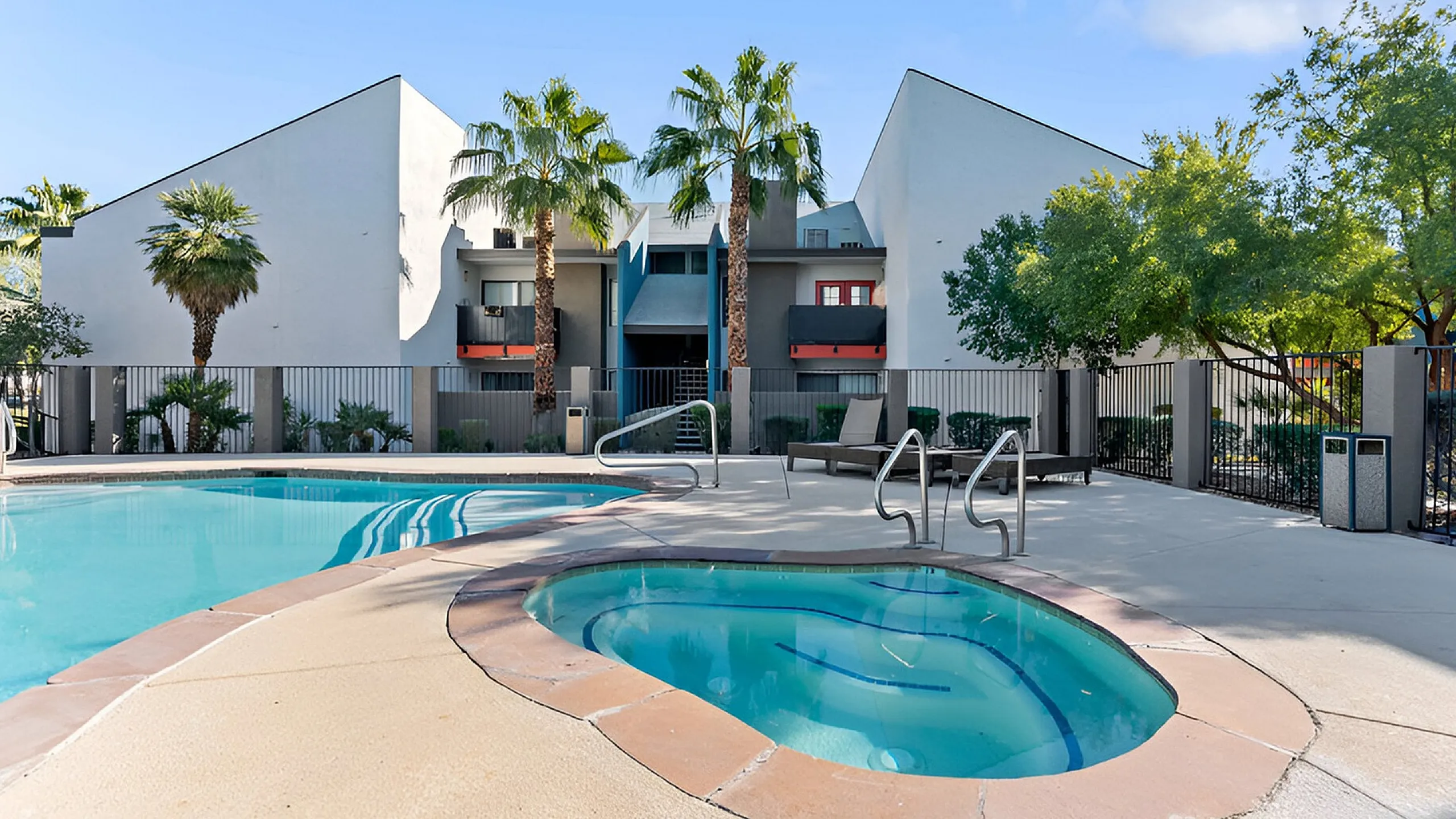 Modern apartment complex with refreshing pool and spa, accented by lush palm trees and vibrant architectural design.