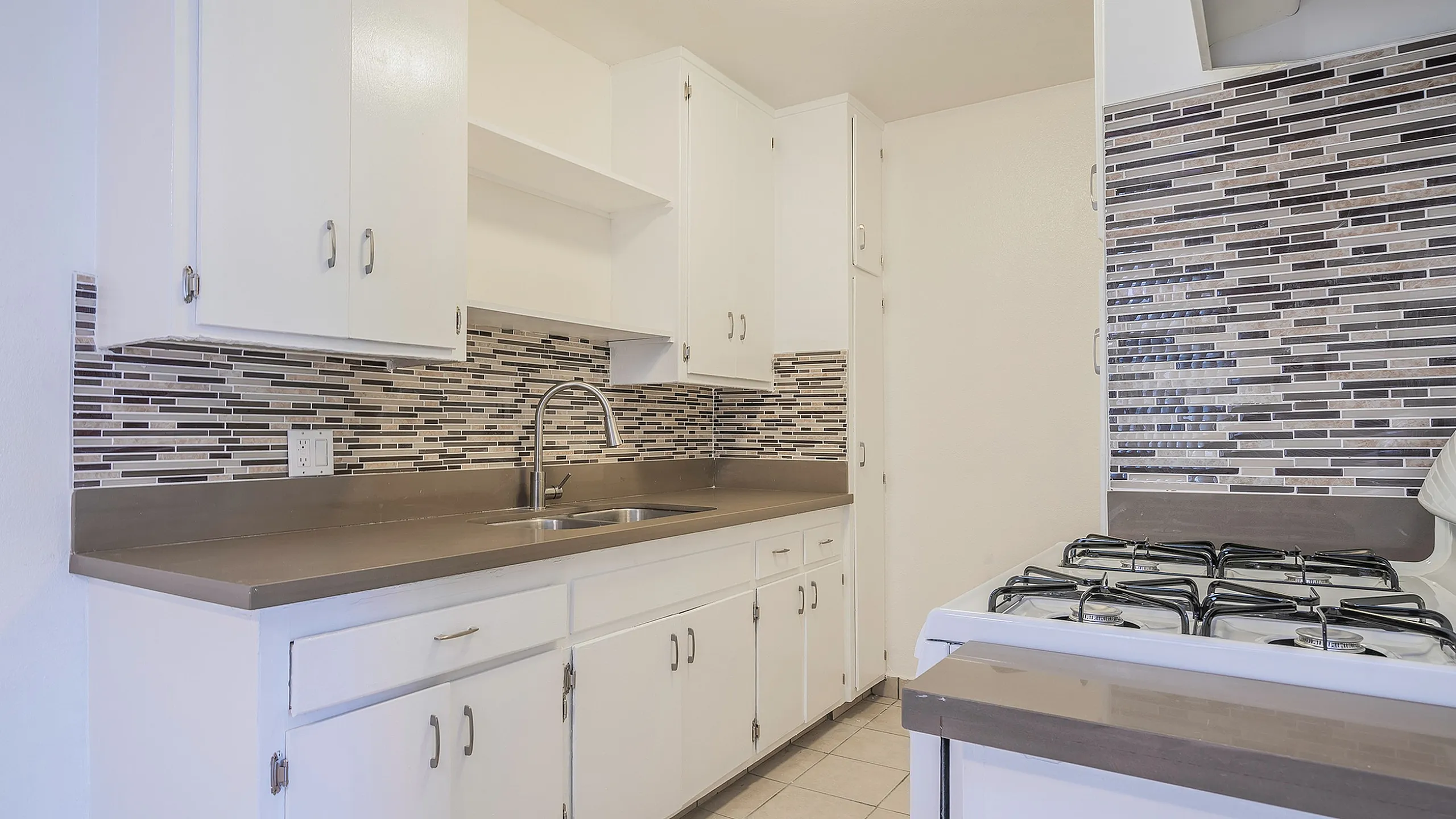 Modern kitchen with sleek countertops, mosaic backsplash, and bright white cabinets.
