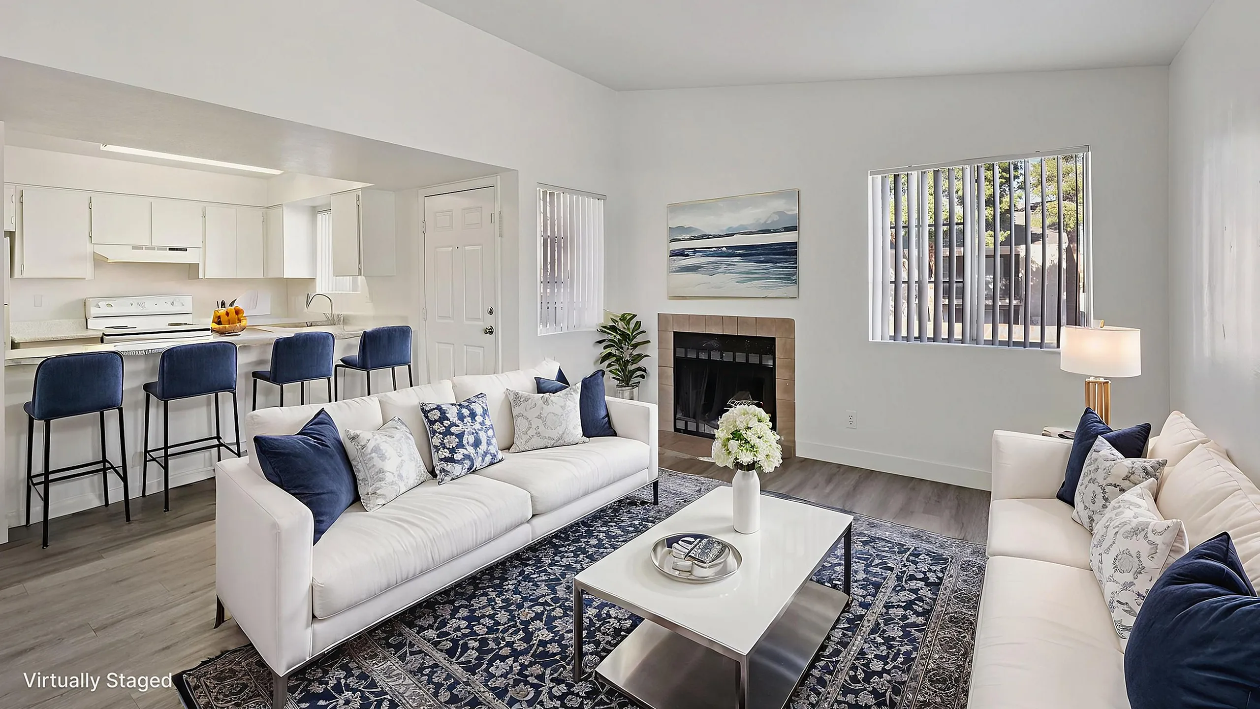 Modern and inviting living space with elegant white sofas, a chic coffee table, and a cozy fireplace. The open-concept layout flows seamlessly into a spacious kitchen with stylish bar seating and sleek appliances. The room is bright and air