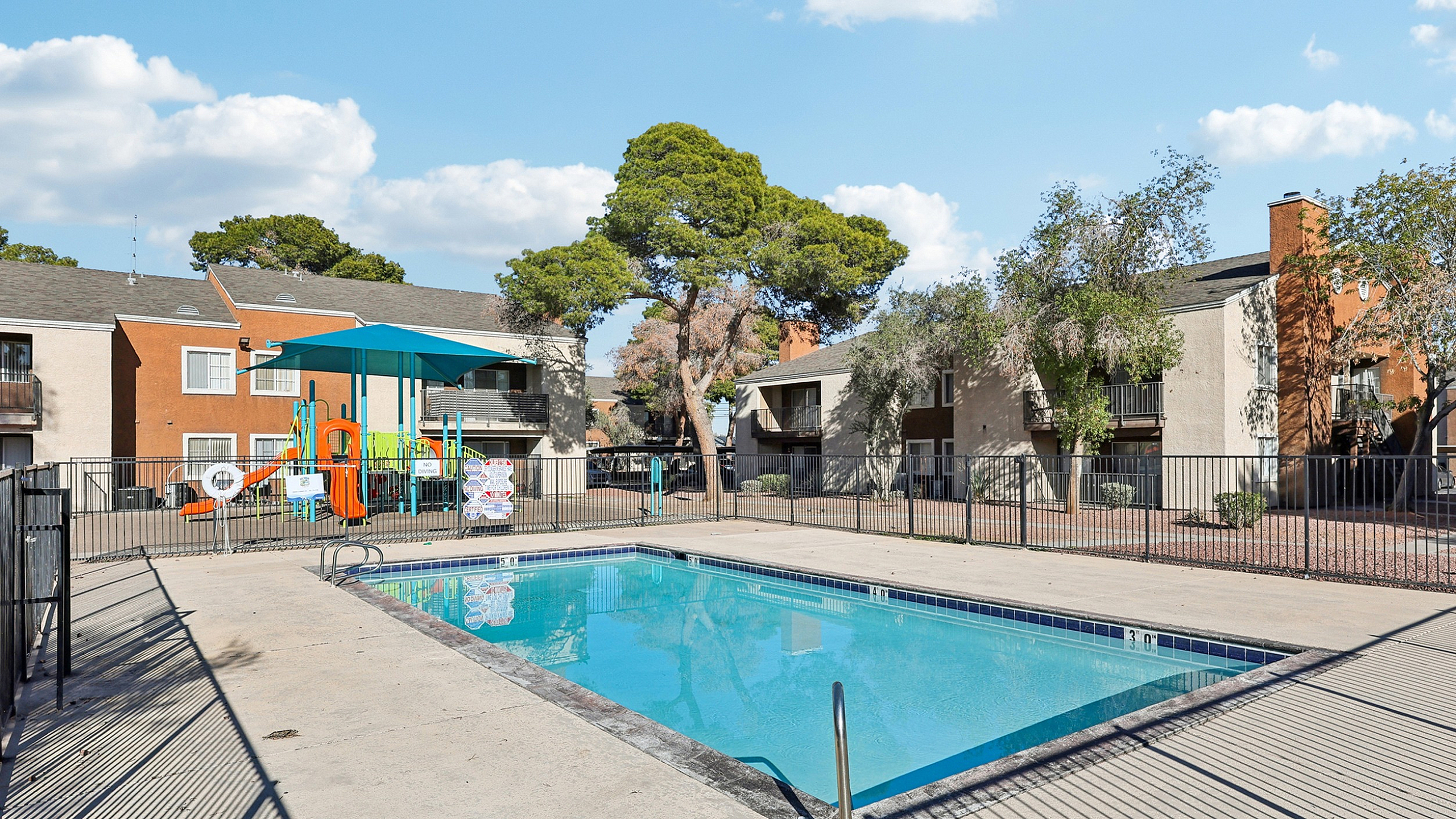 Inviting apartment complex with a sparkling outdoor pool and vibrant playground, perfect for family-friendly living.