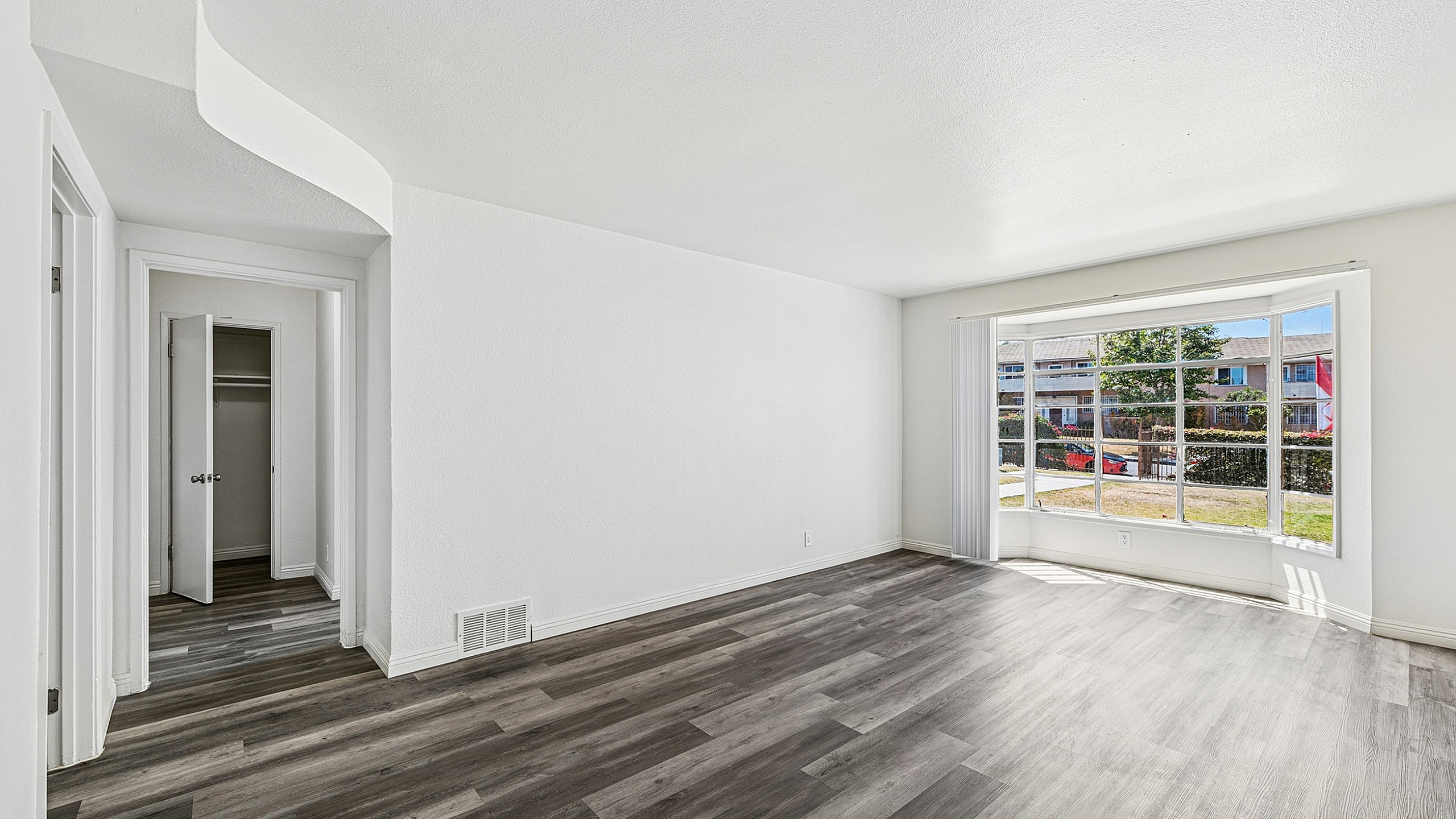 Bright and airy living room with modern hardwood floors, large windows offering natural light, and a closet for convenience.
